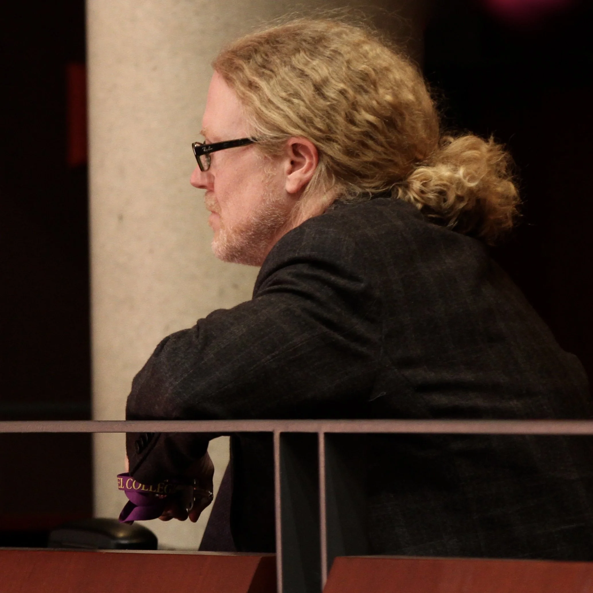 Shawn is a white man with long curly blonde hair who wears black glasses and a dark jacket.