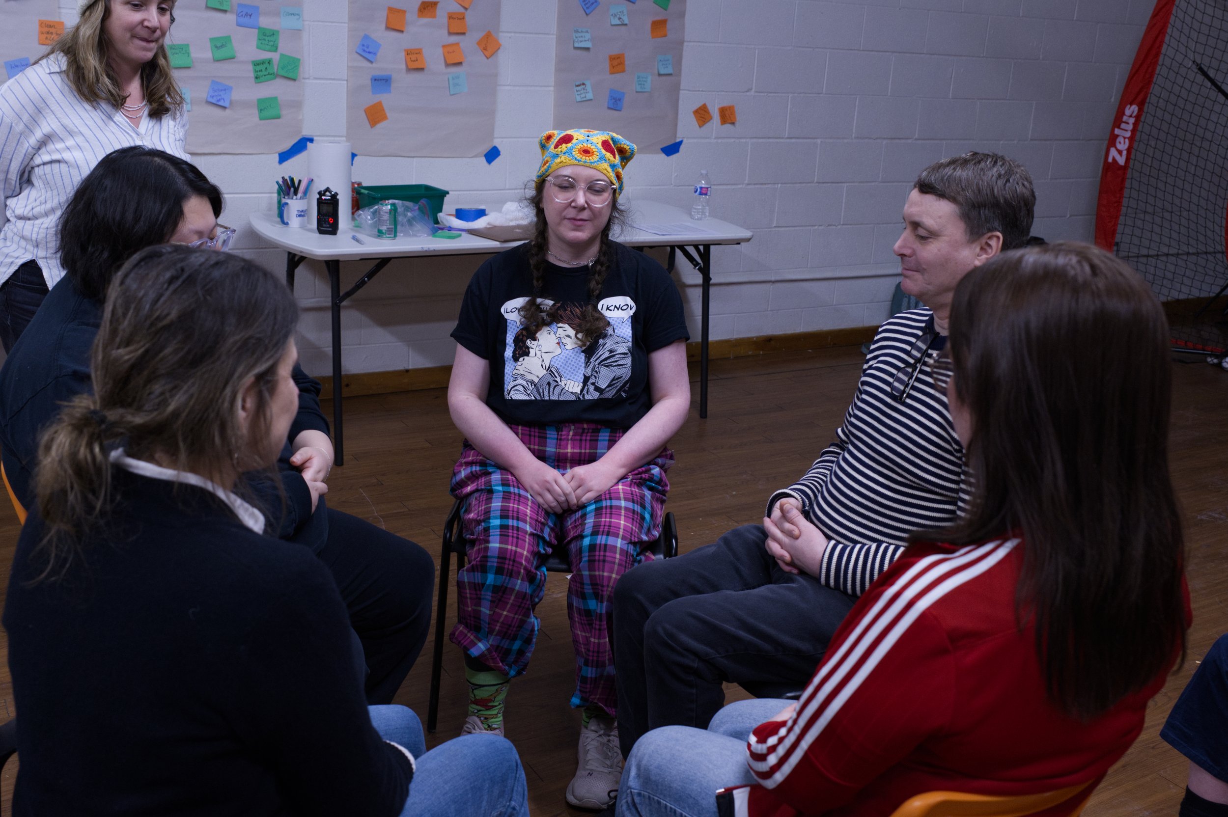 Clockwise from left: Magda, Angela, Lisa (standing), Zoe, Timothy and Sasha, seated in chairs in a circle, playing a game. Photo by Tyler Preece.