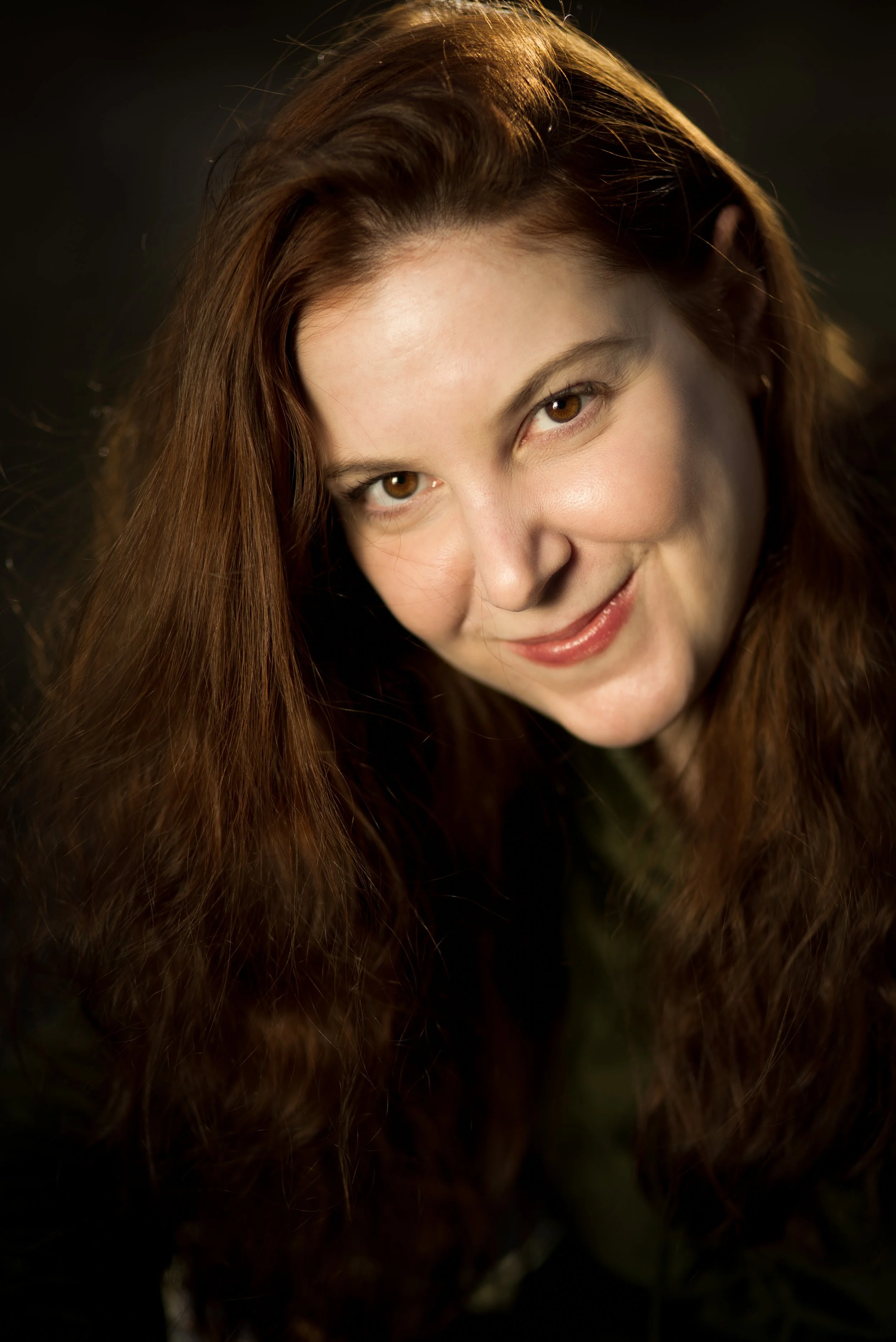 Zoe is a white woman with long auburn hair, who wears a black shirt.