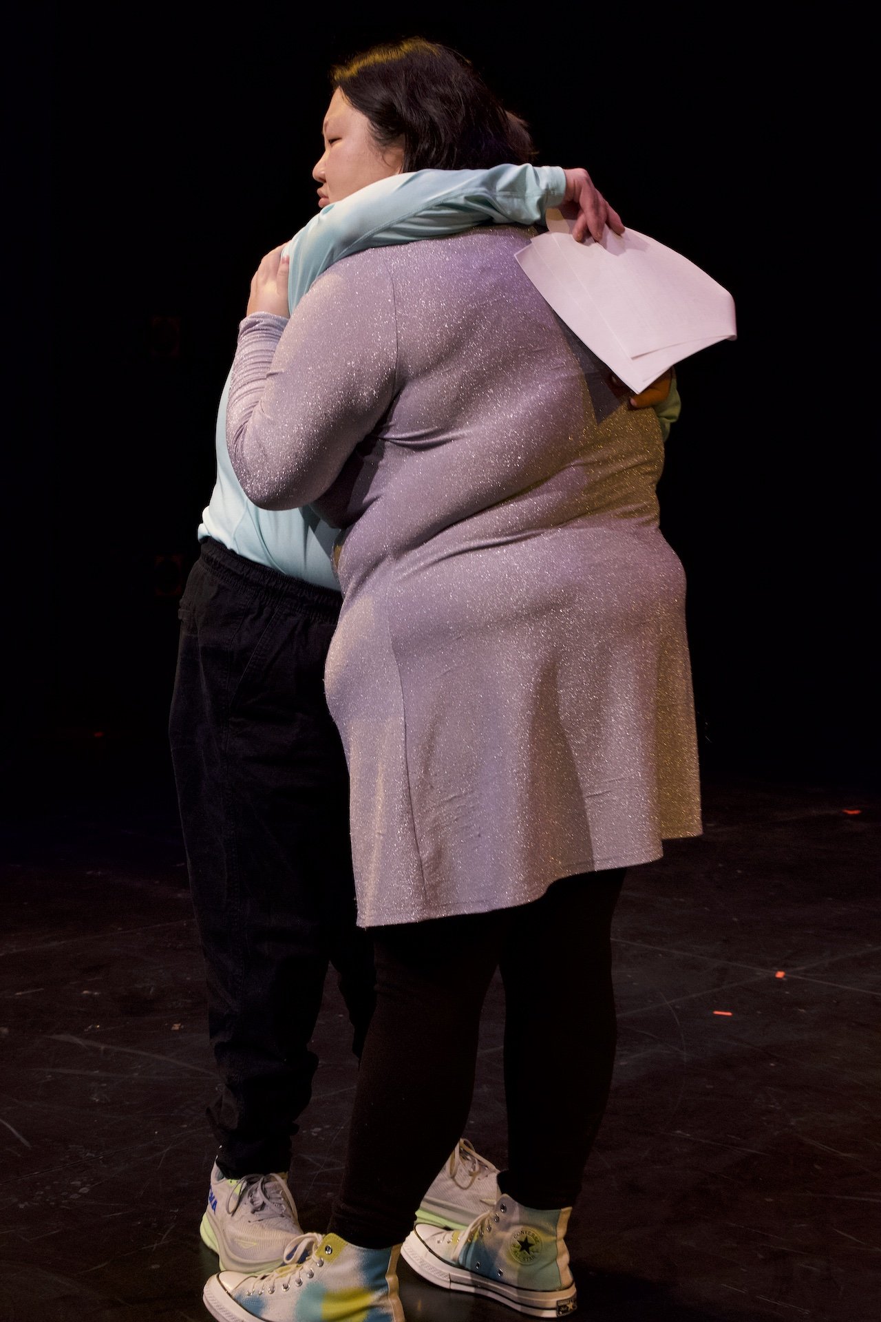 Photo of Angela Sun and Andreas Prinz by Tyler Preece. Andreas and Angela embrace. Andreas wears a long-sleeved blue shirt, black pants and sneakers. Angela wears a sparkly grey/purple dress and white Converse high tops.