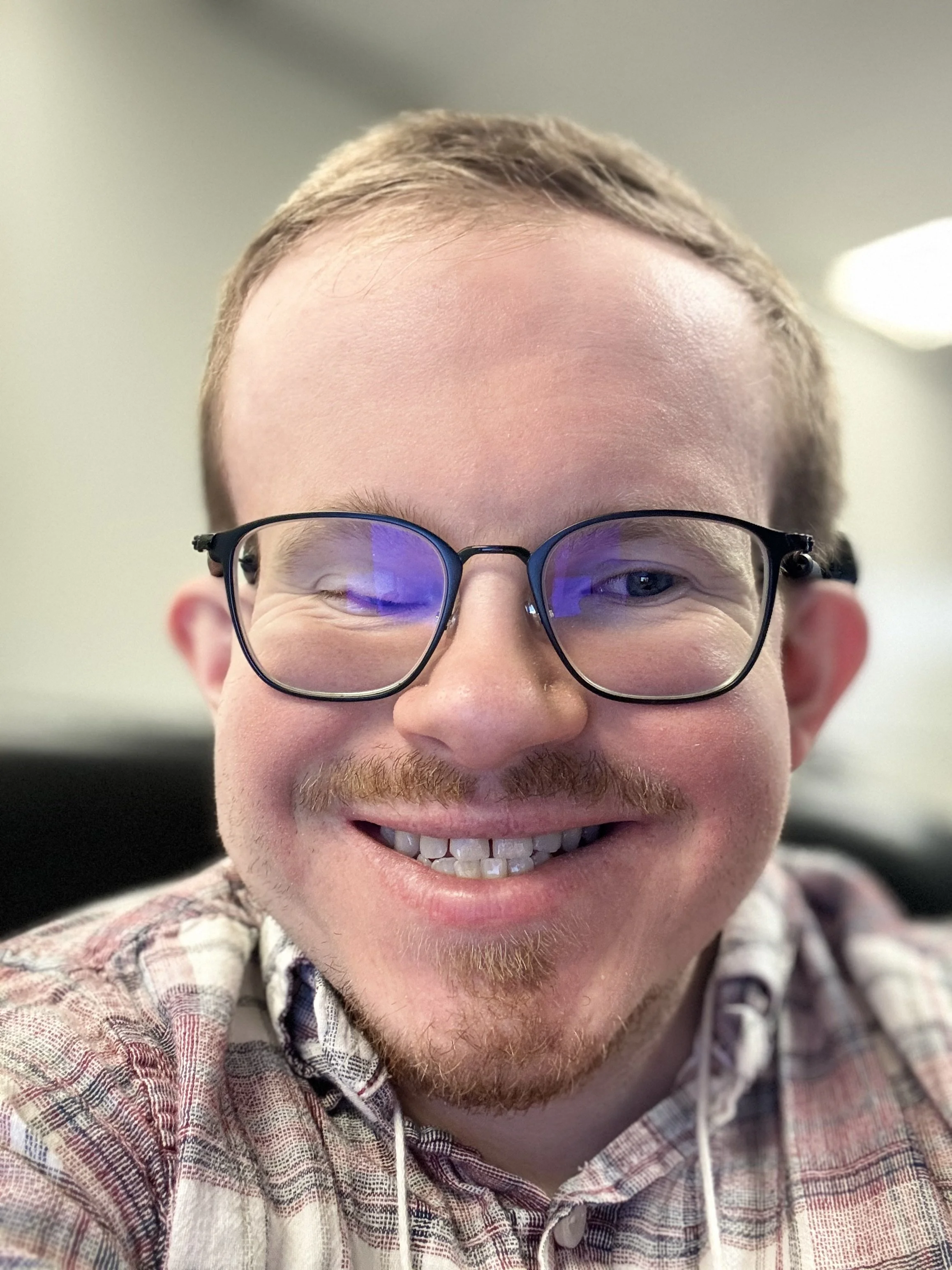 Tyler is a white man with short blonde hair wearing rectangular glasses and a plaid shirt.