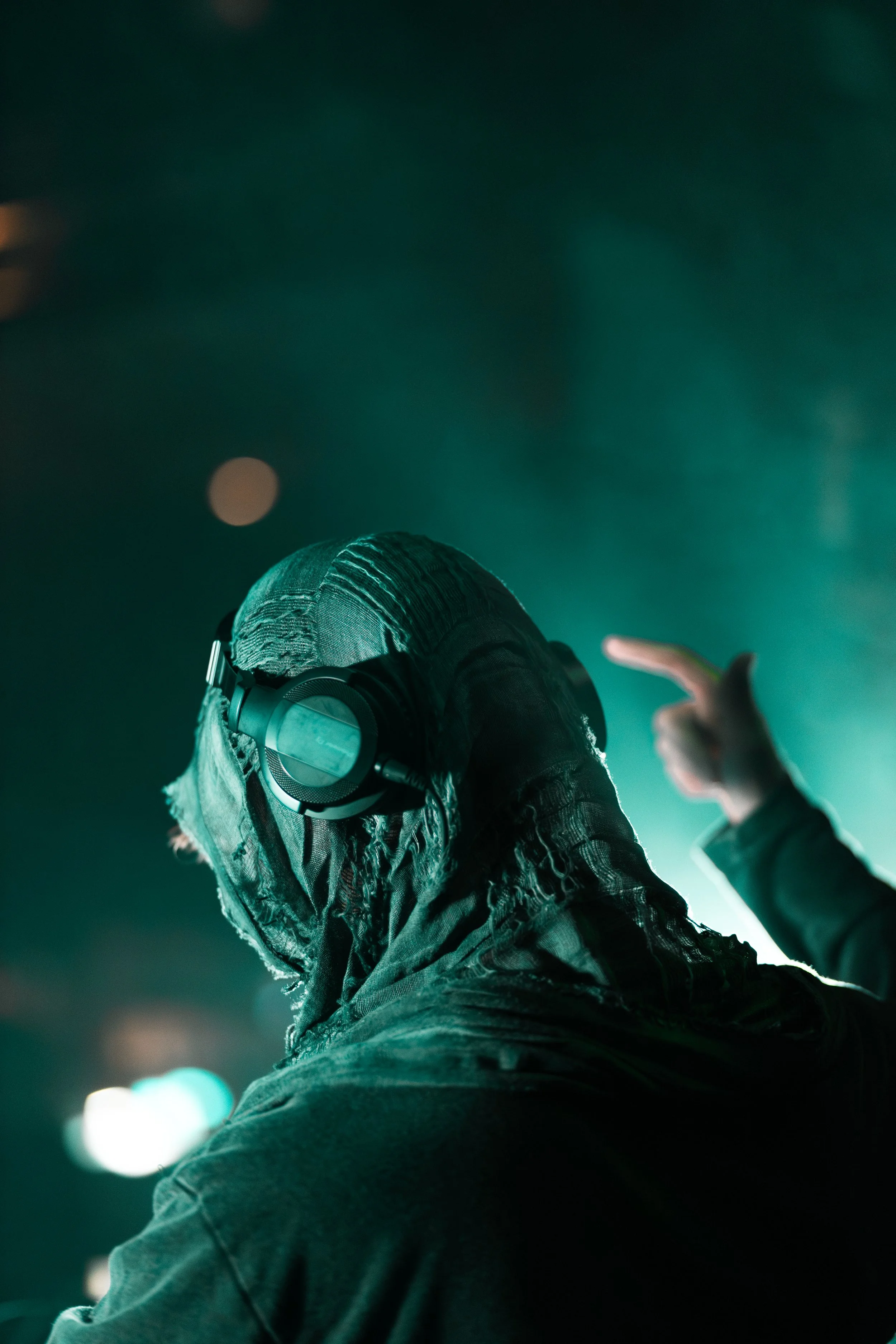 A person wearing headphones with a scarf covering their face, in a dark setting with green lighting.