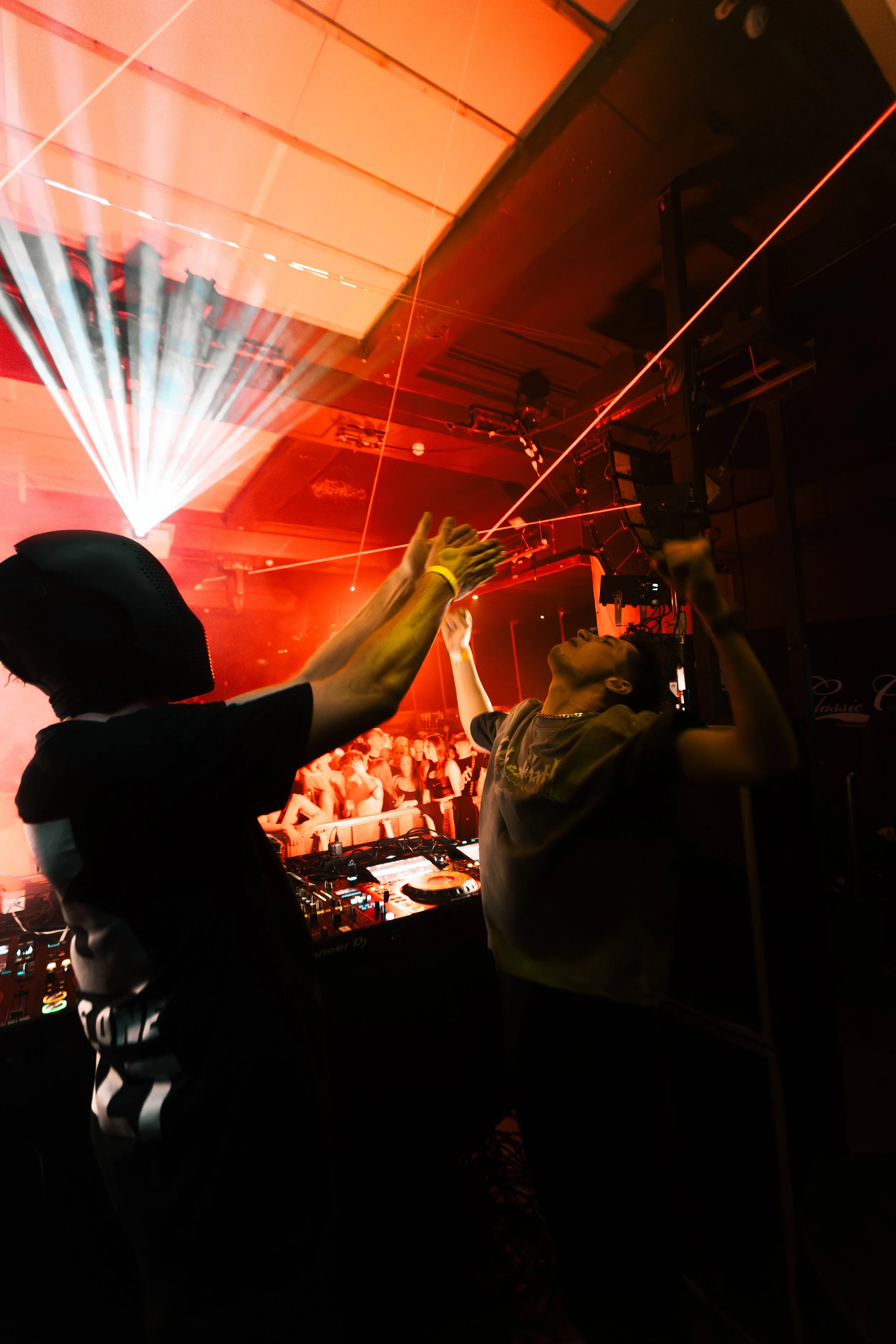Two people dancing in a dark nightclub, with red laser and strobe lights, amid a crowd of partygoers.