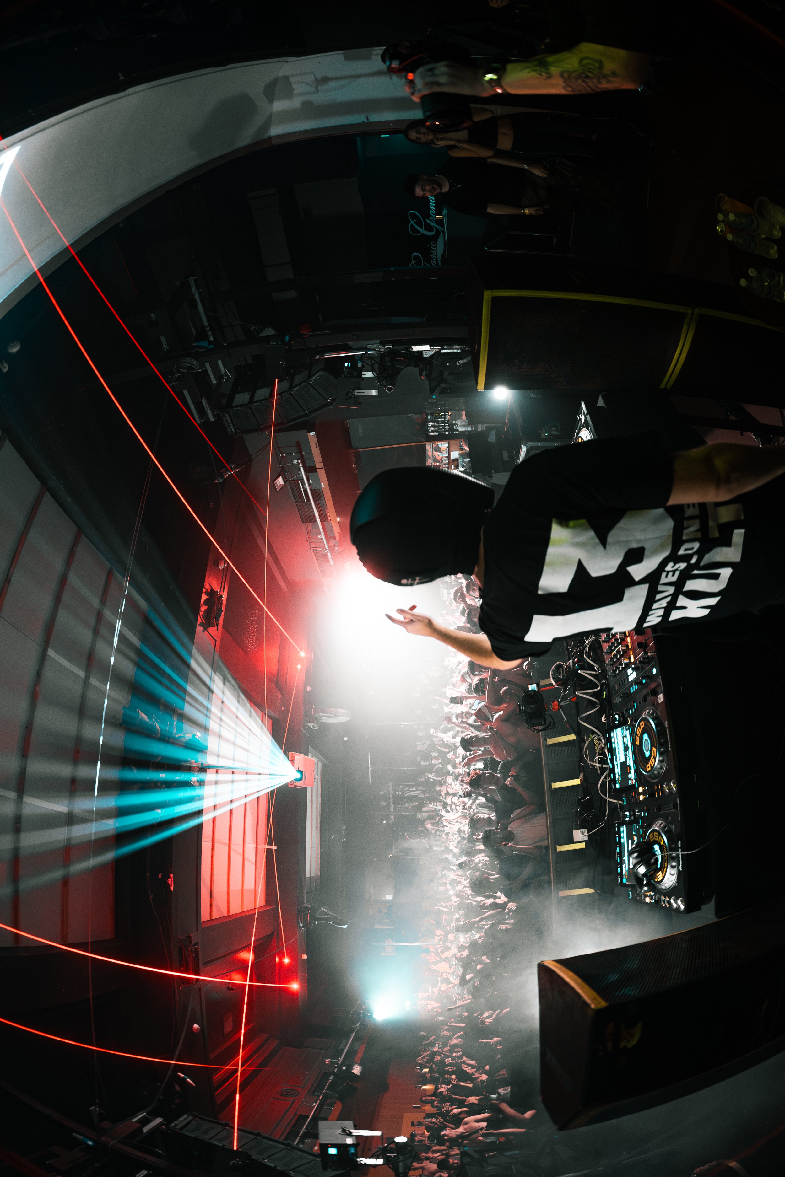 A DJ performing at a nightclub with laser lights and a crowd dancing.
