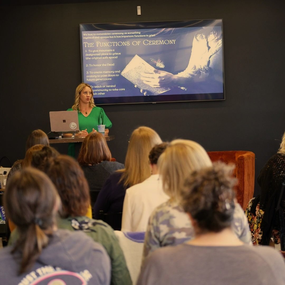 A speaker in a green dress giving a presentation to an audience, with a screen displaying a slide titled "The Functions of Ceremony."