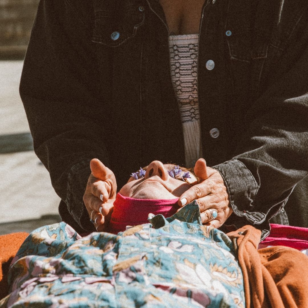 Person lying down wearing a floral jacket with flowers on eyes; hands positioned near head.