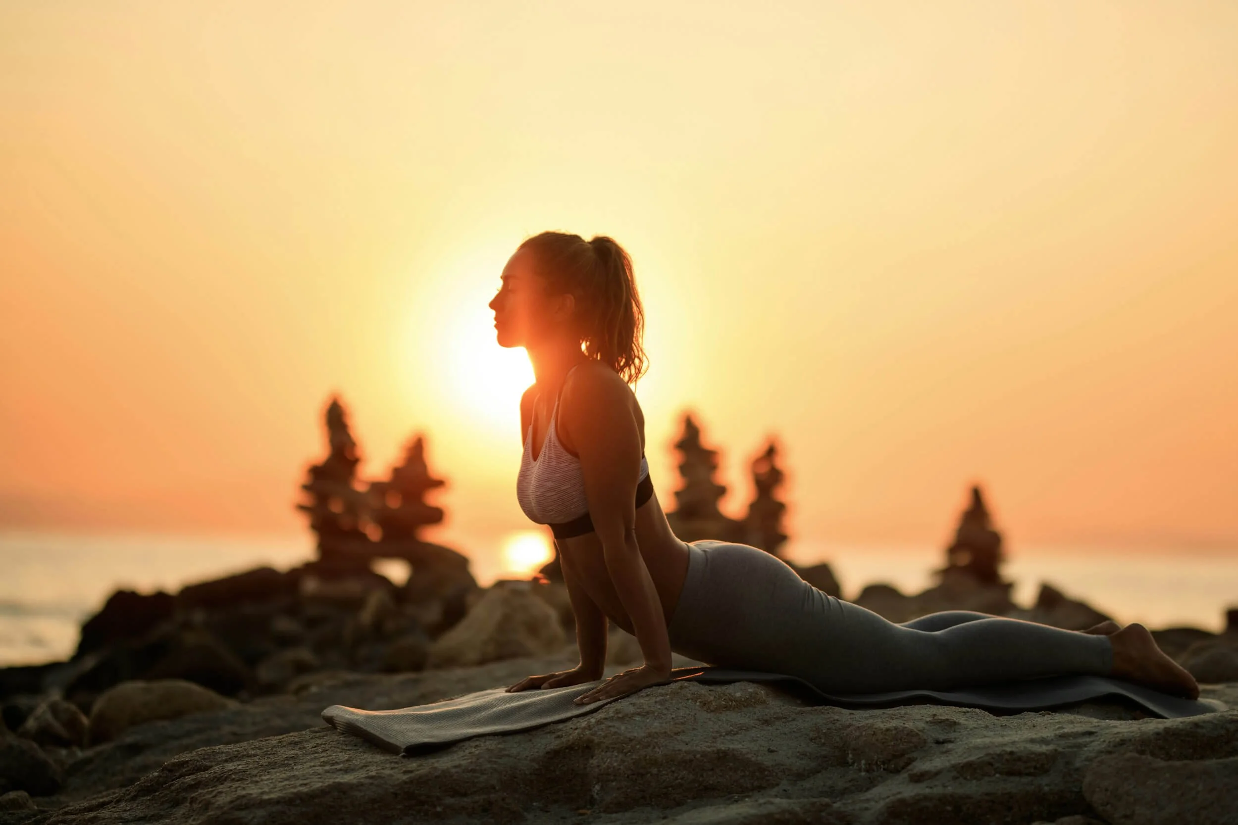 Woman practicing yoga in cobra pose on a beach at sunset.
