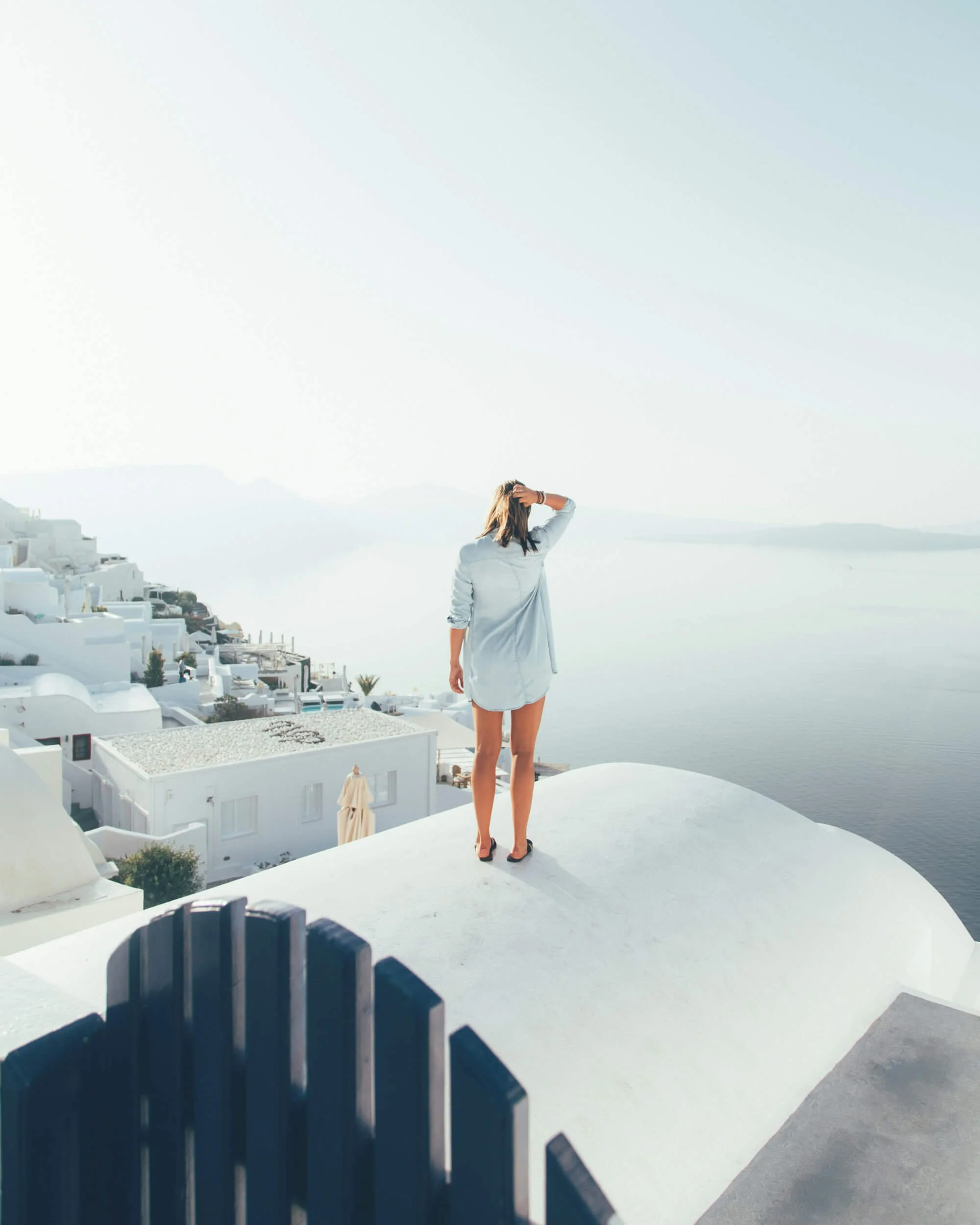 Woman standing on white rooftop overlooking sea and white buildings in Santorini, Greece.