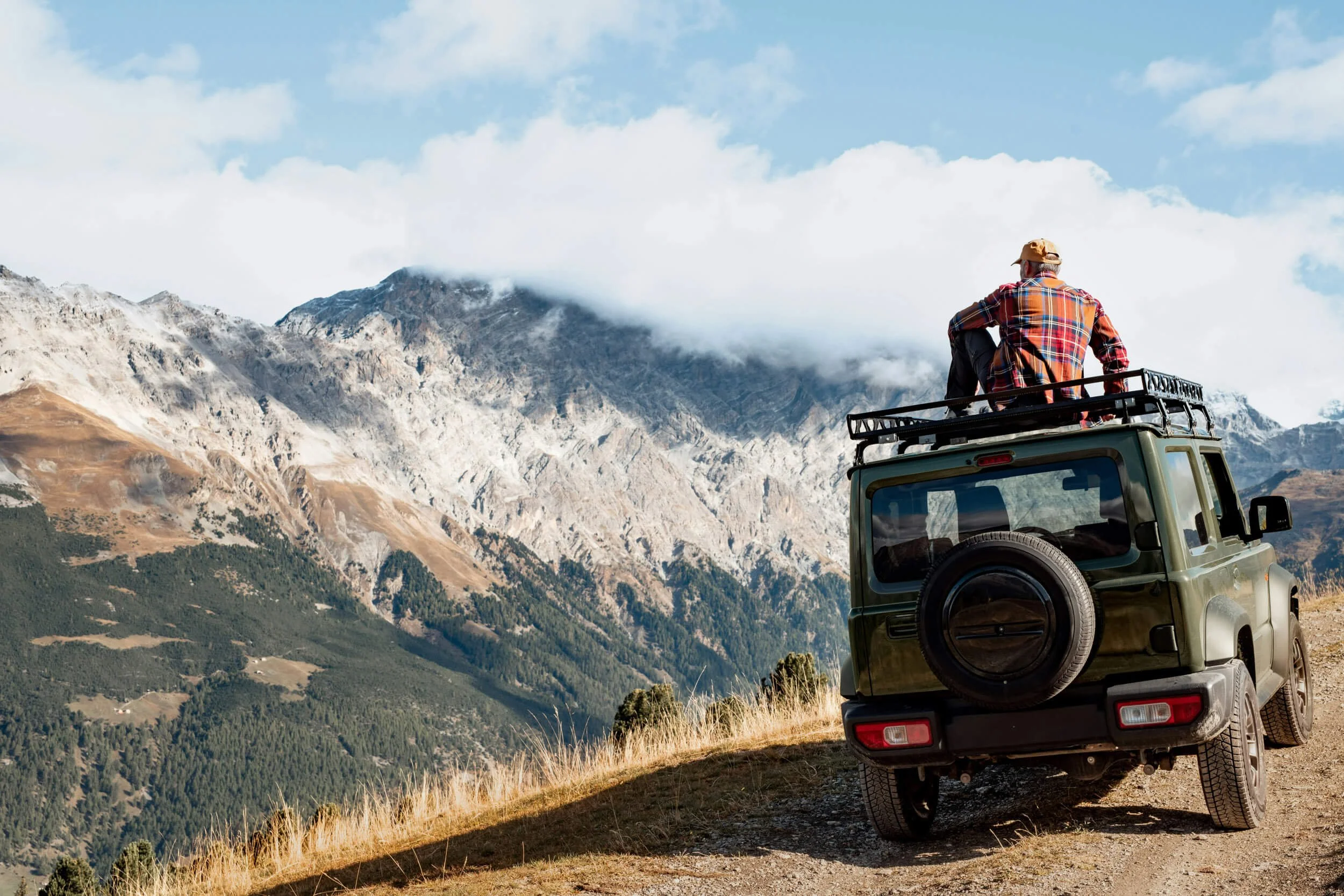 Man sitting on SUV roof looking at mountains in nature.