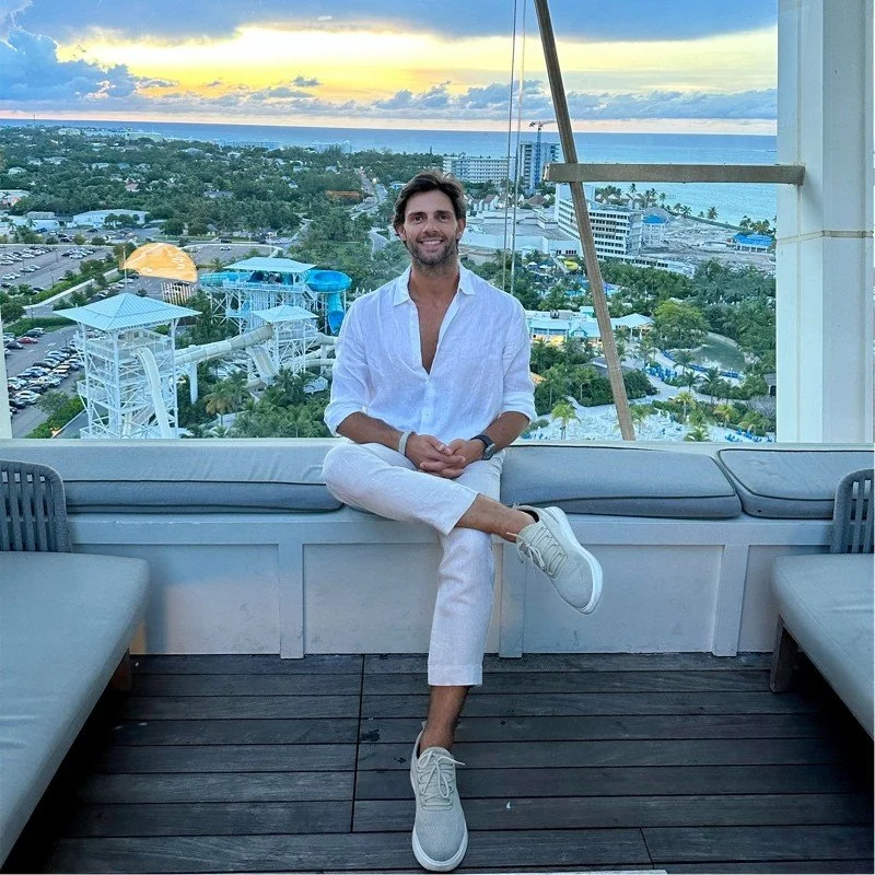 Person sitting on rooftop with city and waterpark view at sunset.