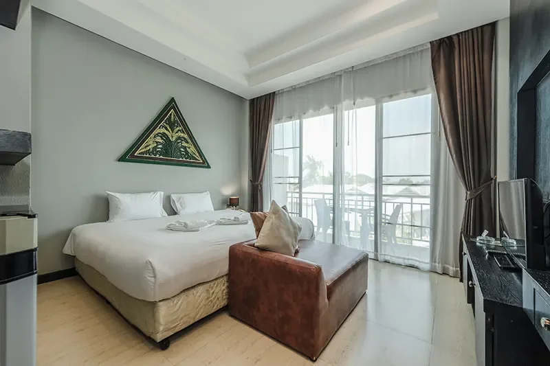 Modern hotel room with a large bed, a sitting lounge, a balcony with outdoor seating, and a flat-screen TV.