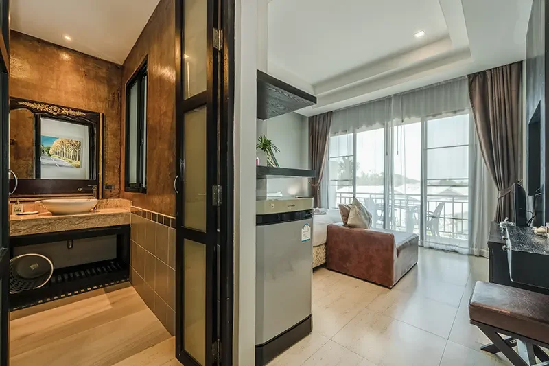 View of a living room with a sofa, glass door balcony, and a television, adjacent to a bathroom with a sink, mirror, and window.