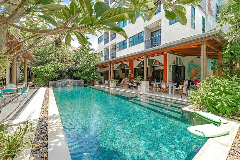 Luxury poolside area at a hotel or resort with lounge chairs, greenery, and a modern building background.