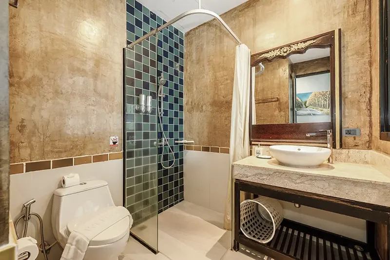 Bathroom with a toilet, shower area with glass door, sink on a stone countertop, and a large mirror above the sink.