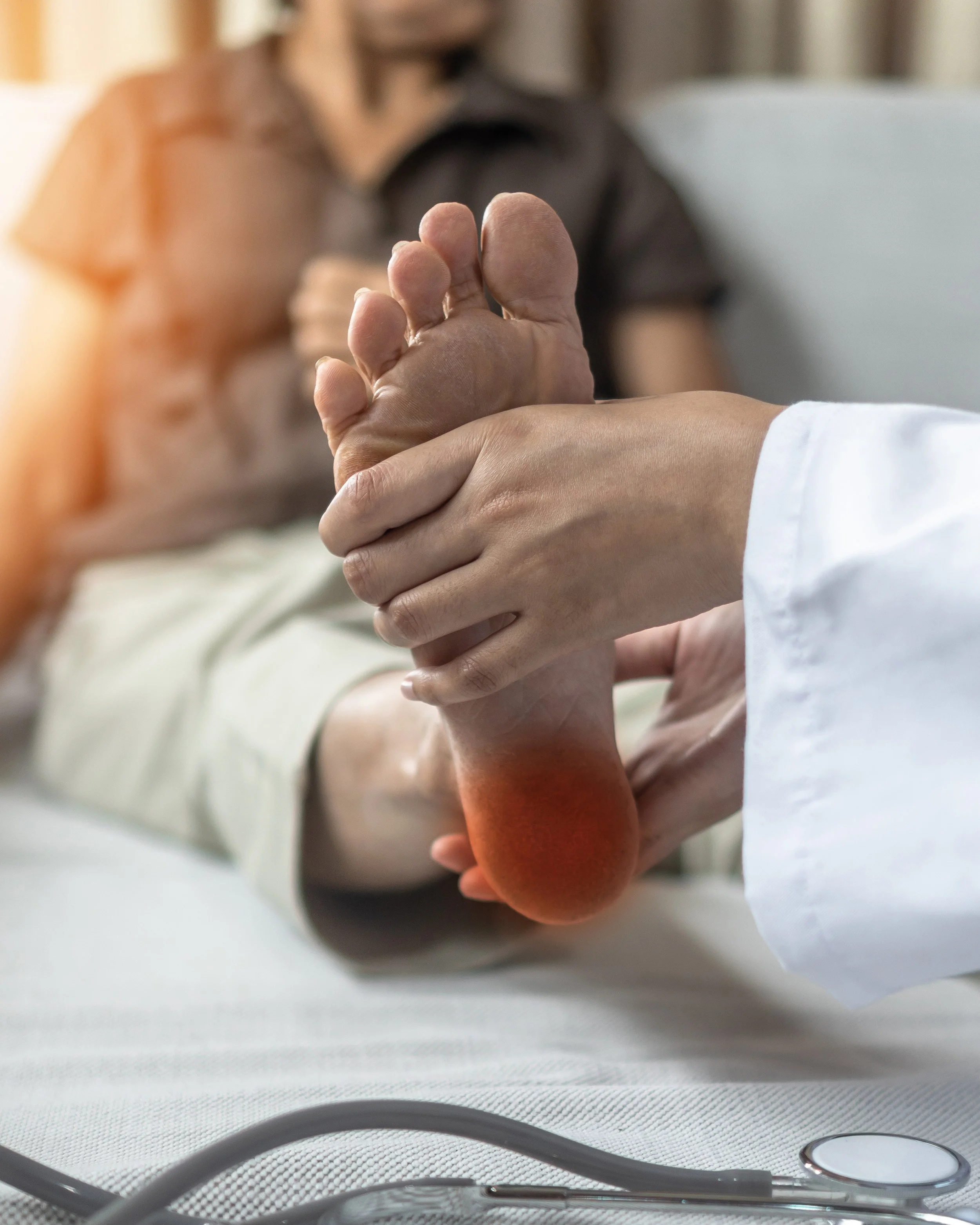 A healthcare professional holds an elderly patient's foot during a medical examination in a hospital room.