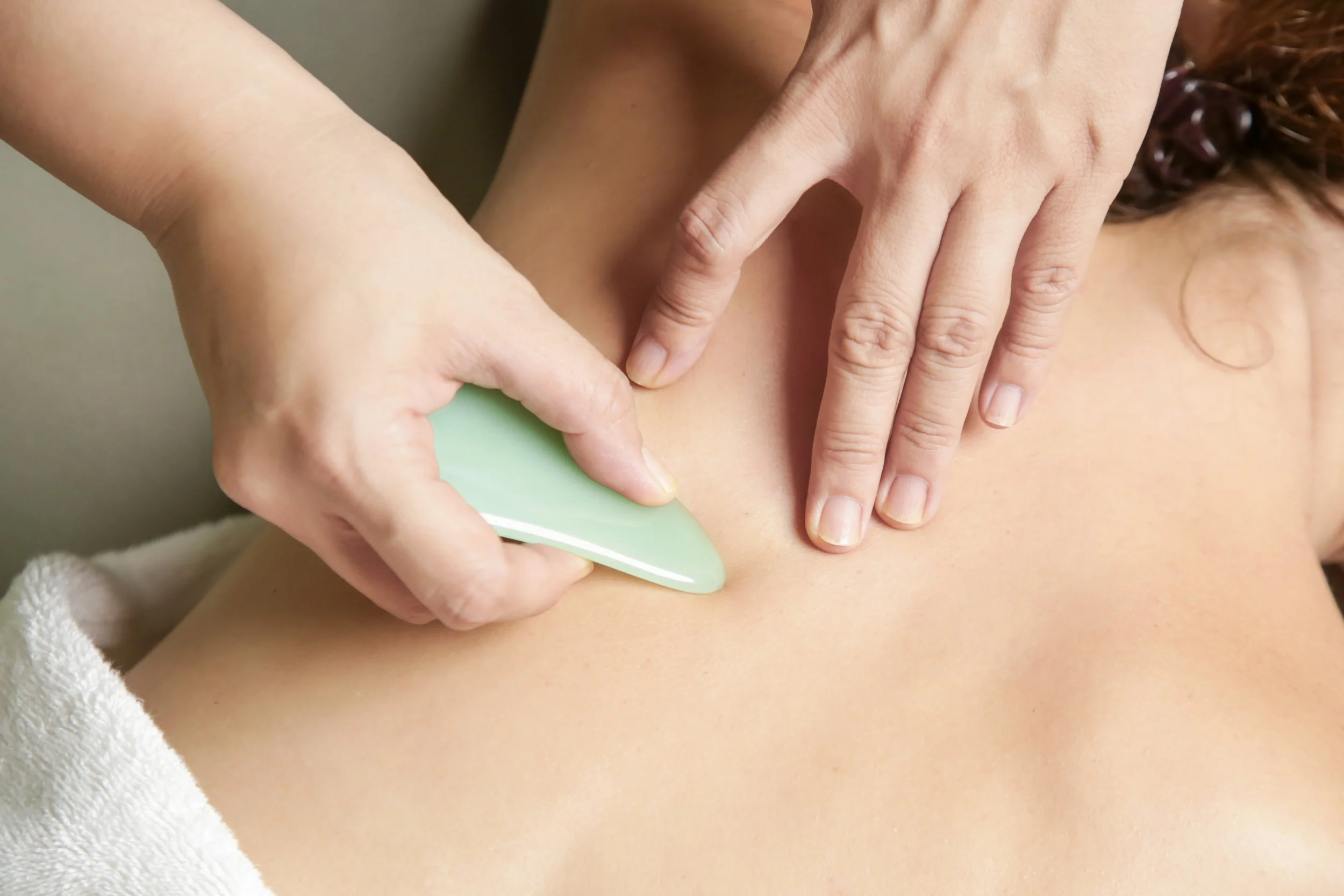 A person receiving a massage with a jade roller on their upper back.
