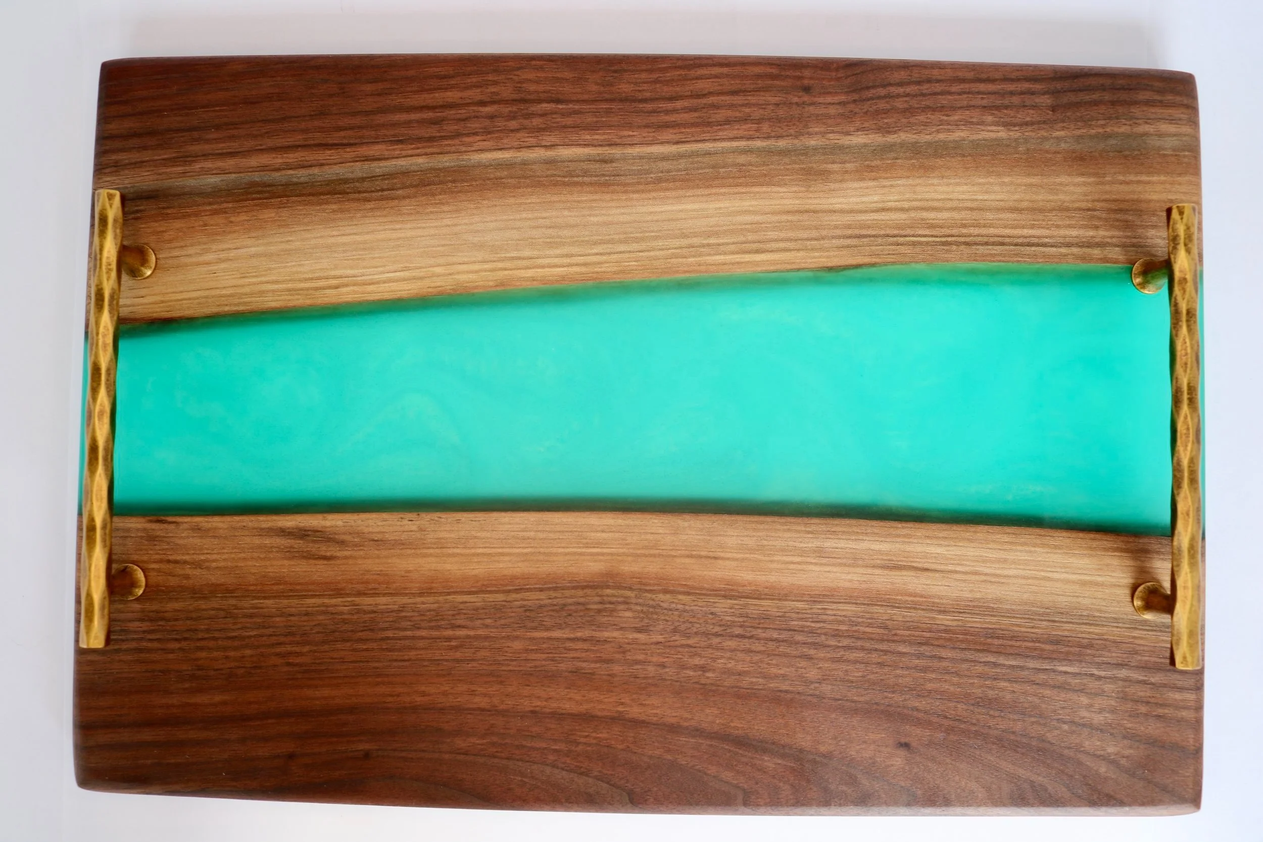 Handmade black walnut serving board with a vibrant turquoise blue epoxy resin river design and unique textured gold metal handles, ideal for display and serving food.