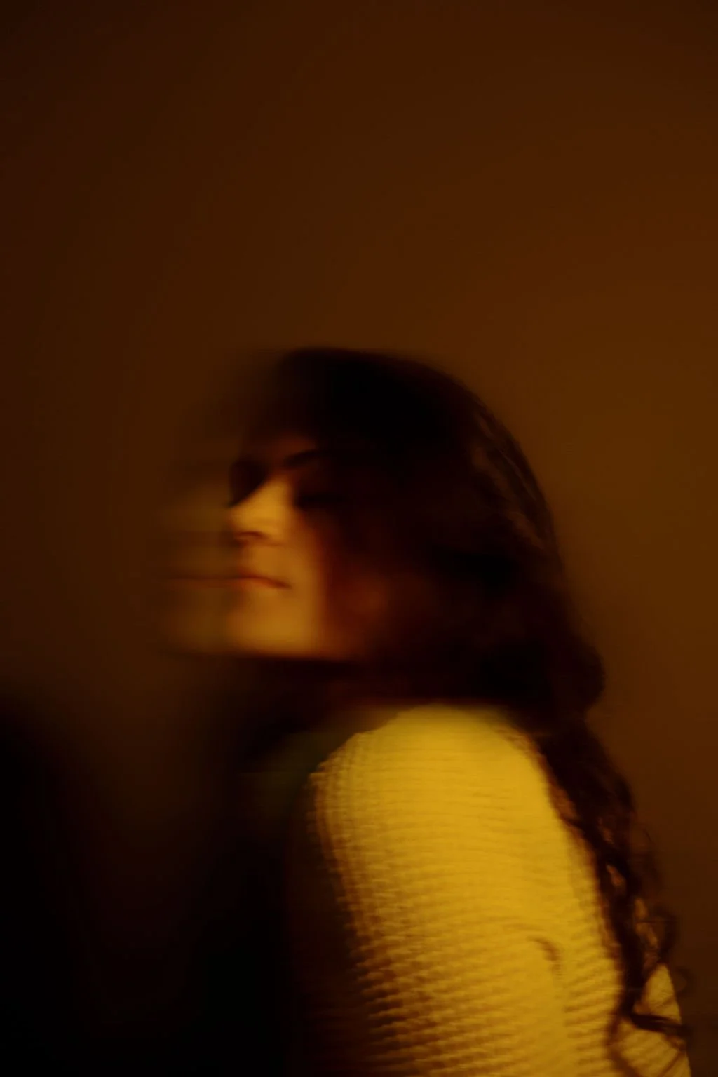 A woman with long, wavy hair looking over her shoulder in a dimly lit environment.