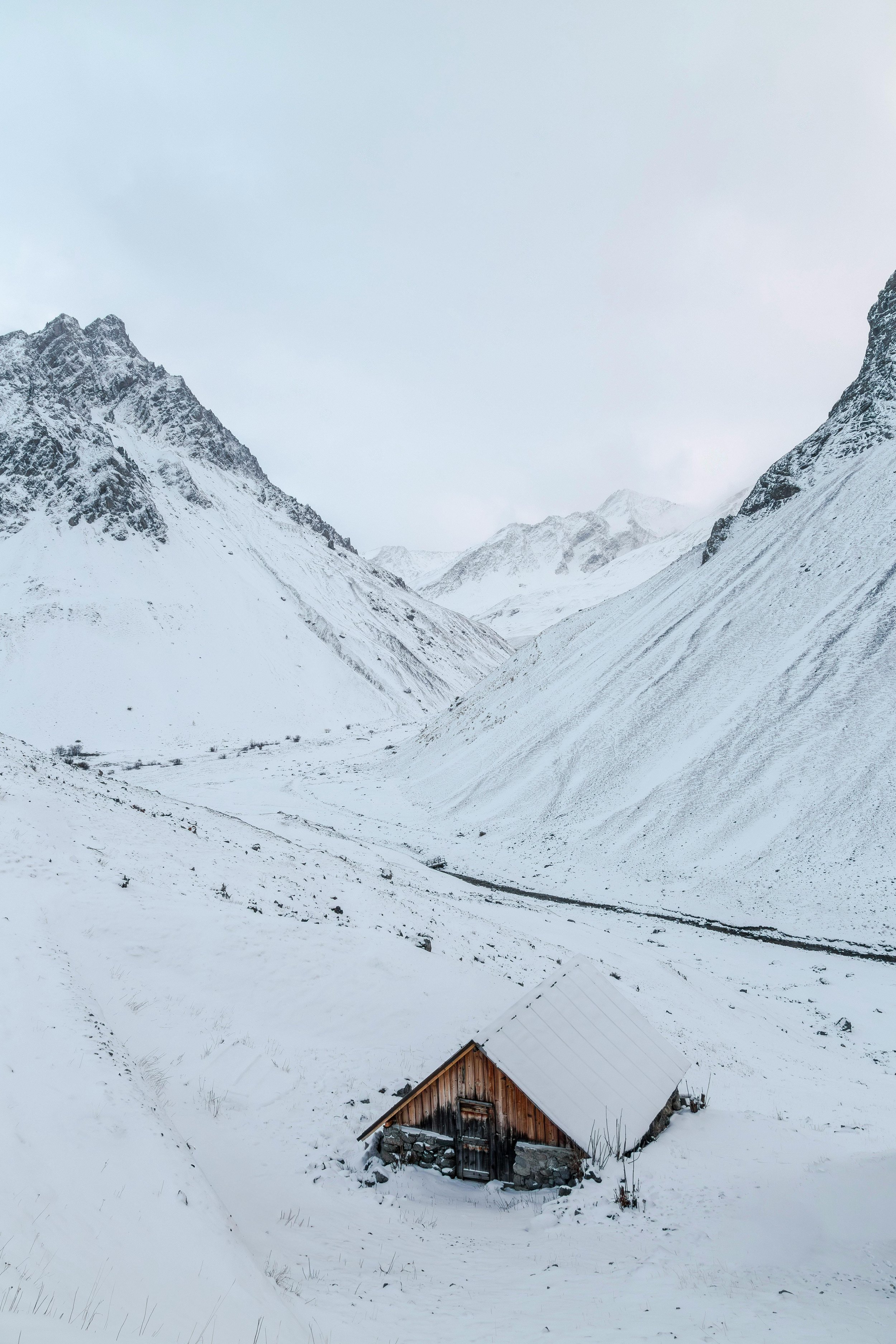Snow-covered mountains with a small rustic wooden cabin in the valley.