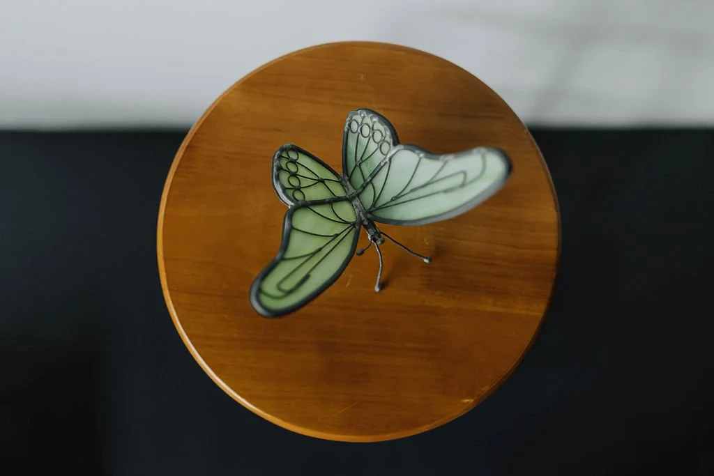 Decorative butterfly-shaped lamp with green and black outlined wings on a round wooden surface.