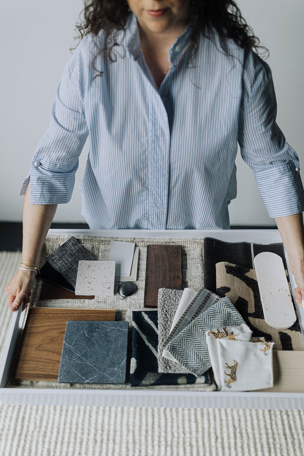 Anna Kuttel in a striped blue shirt standing over a table with fabric and material samples for interior design or home decor.