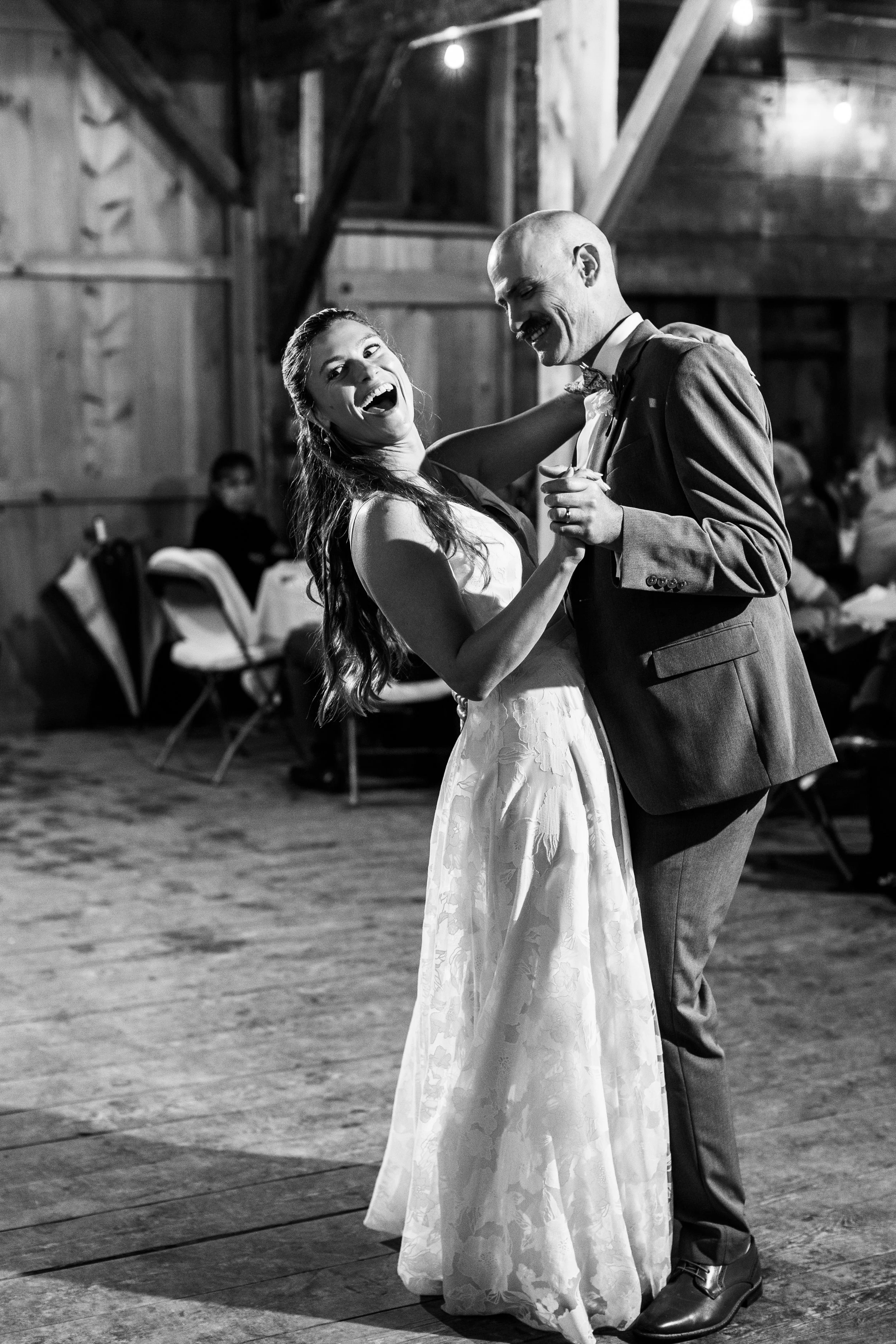 A happy bride and groom dancing at their wedding reception in a rustic wooden venue, smiling and enjoying the moment.