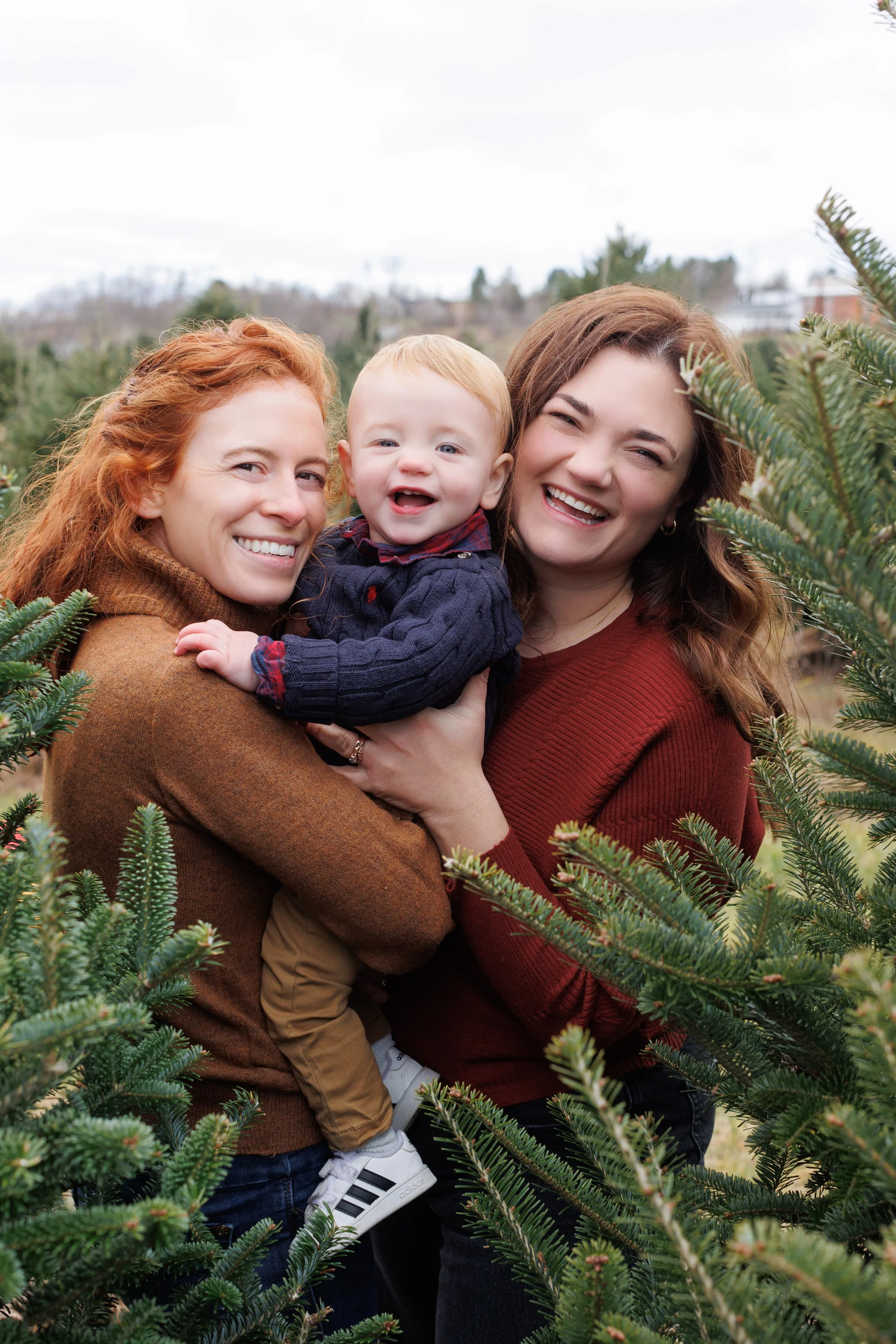 two women and their baby smiling between trees during a vermont mini session
