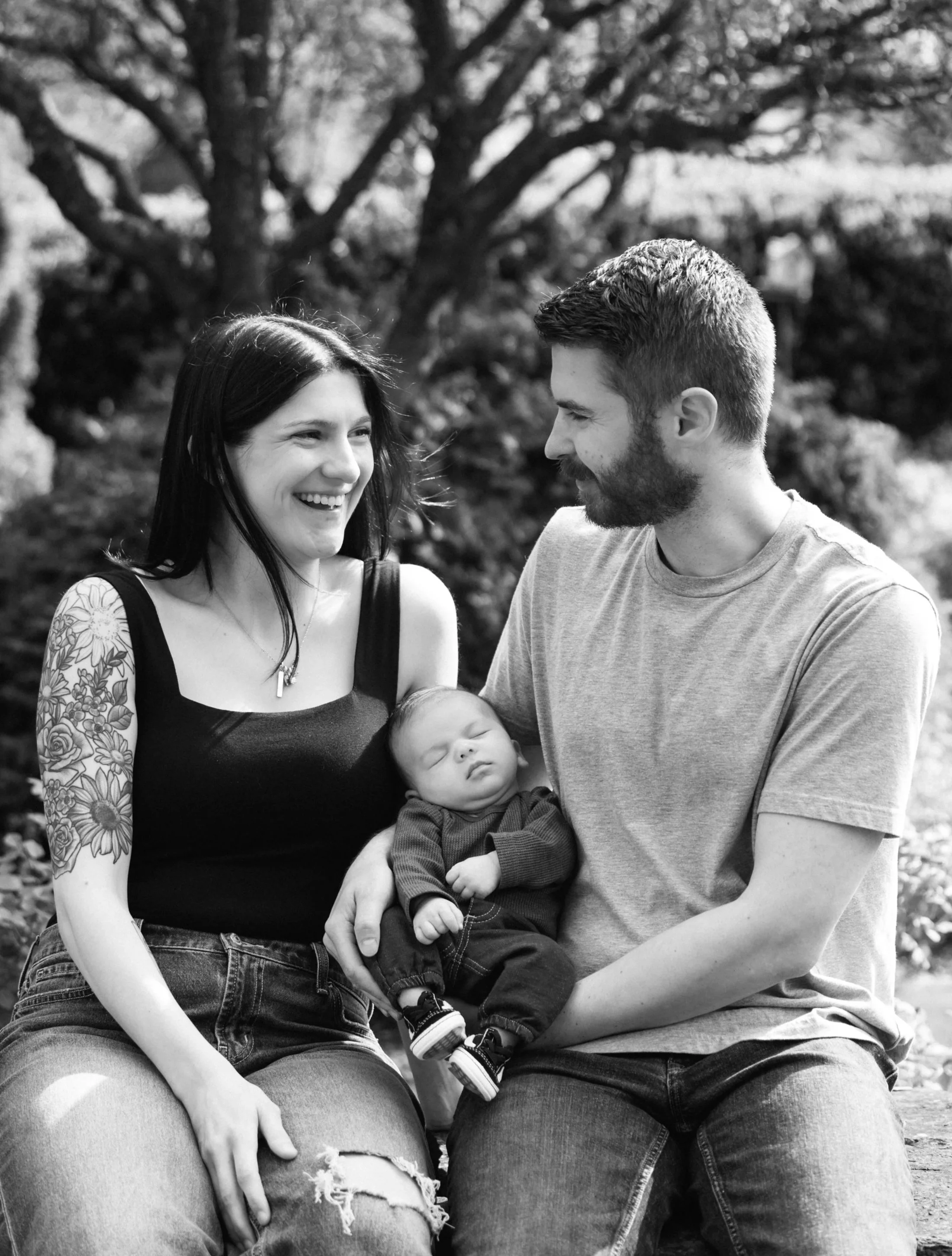 A couple and their newborn sitting on a rock wall and smiling