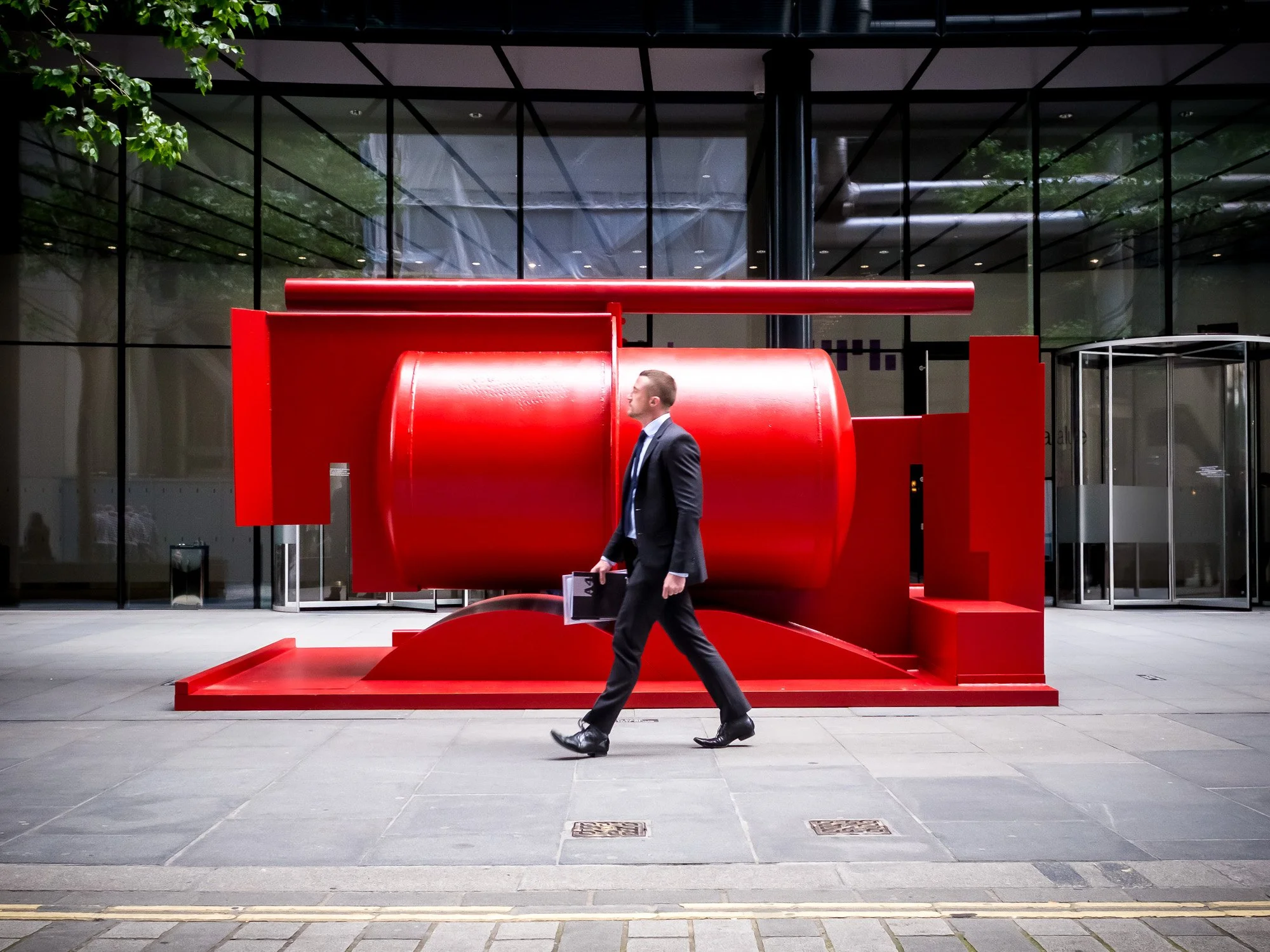 Homme d'affaires marchant devant une installation artistique rouge à l'extérieur d'un bâtiment moderne en verre.