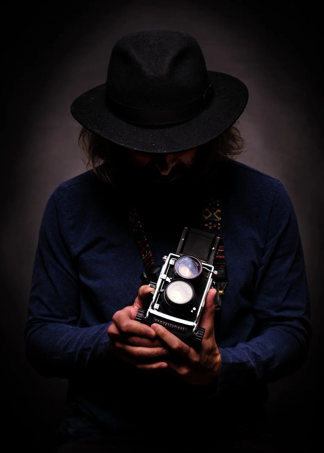 Homme portant un chapeau noir, tenant un appareil photo vintage dans ses mains, fond sombre