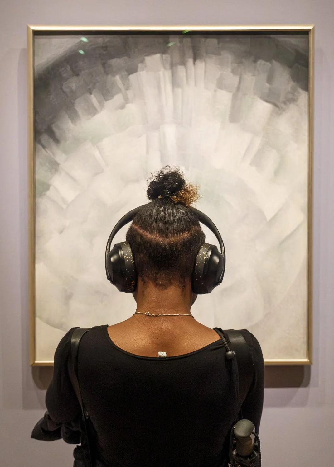 Une femme vue de dos portant un casque audio, regardant une peinture abstraite dans une galerie d'art.