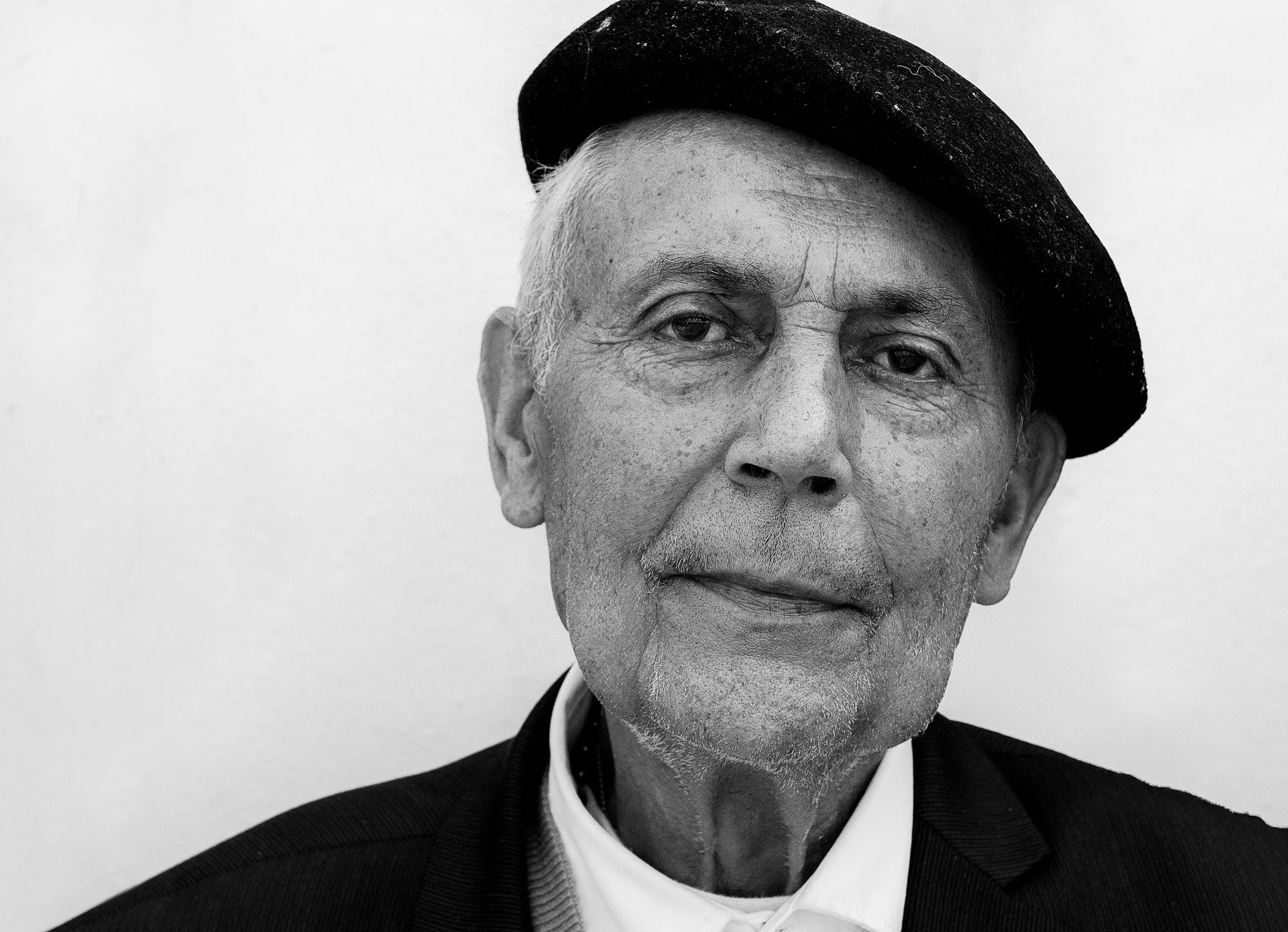 Portrait en noir et blanc d'un homme âgé portant un costume et un béret noir, regardant légèrement à gauche.