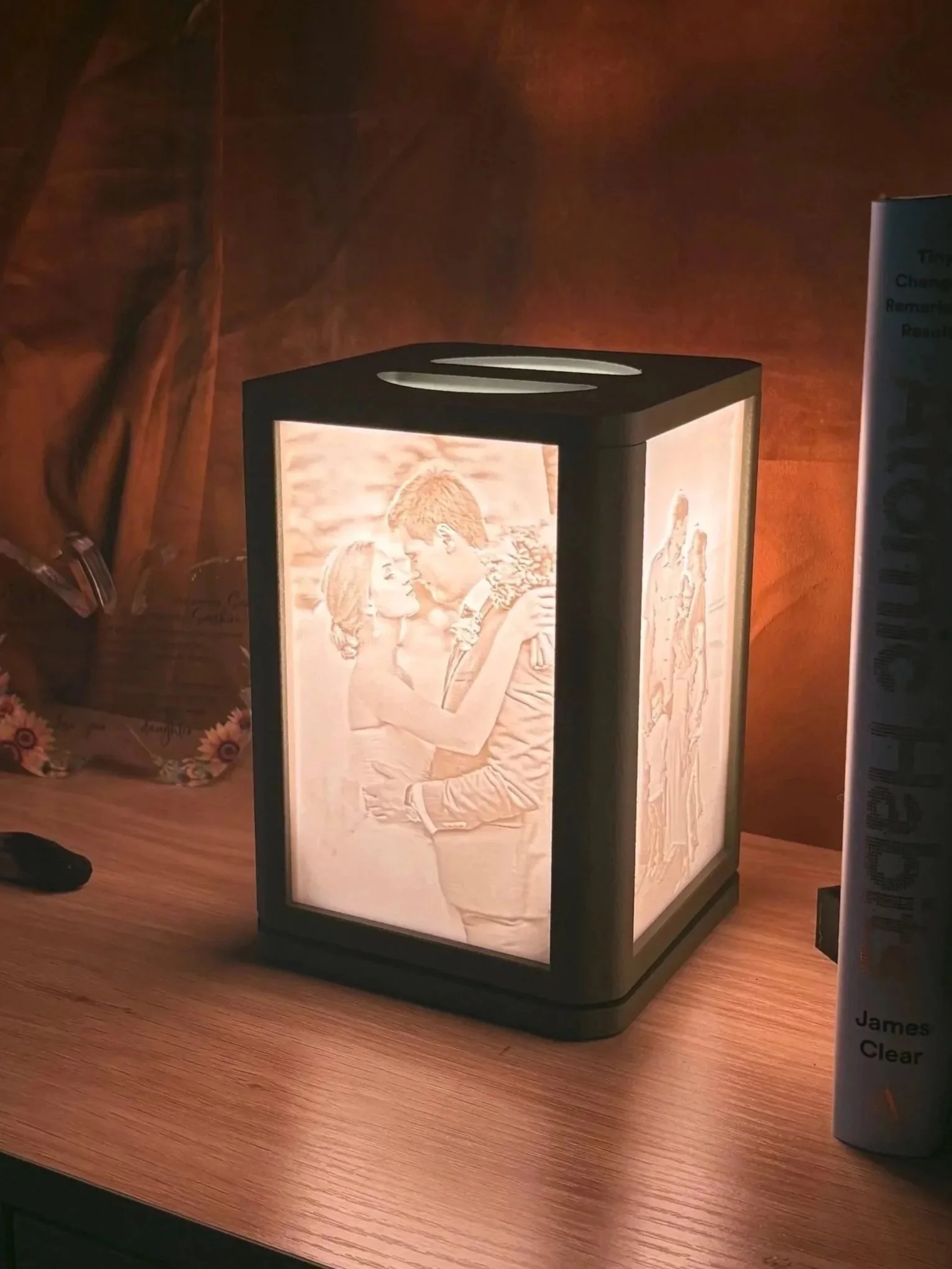 A close-up of a hand adjusting a table lamp with a rectangular shade, featuring printed images of two smiling dogs, on a decorative table with a clock and jewelry.