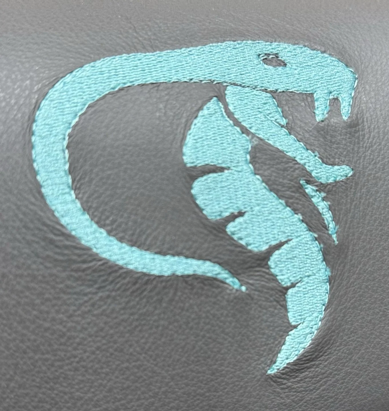 A turquoise embroidered snake design on grey fabric.