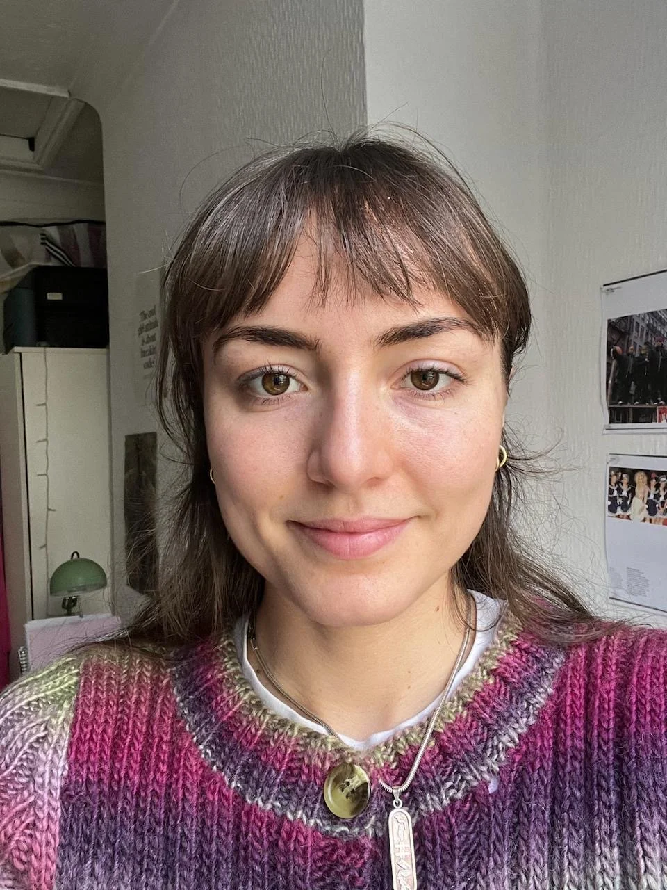 A young woman dressed in a school uniform holding a bouquet of white and pink flowers outside on a cobblestone path, with students and cars in the background during fall.