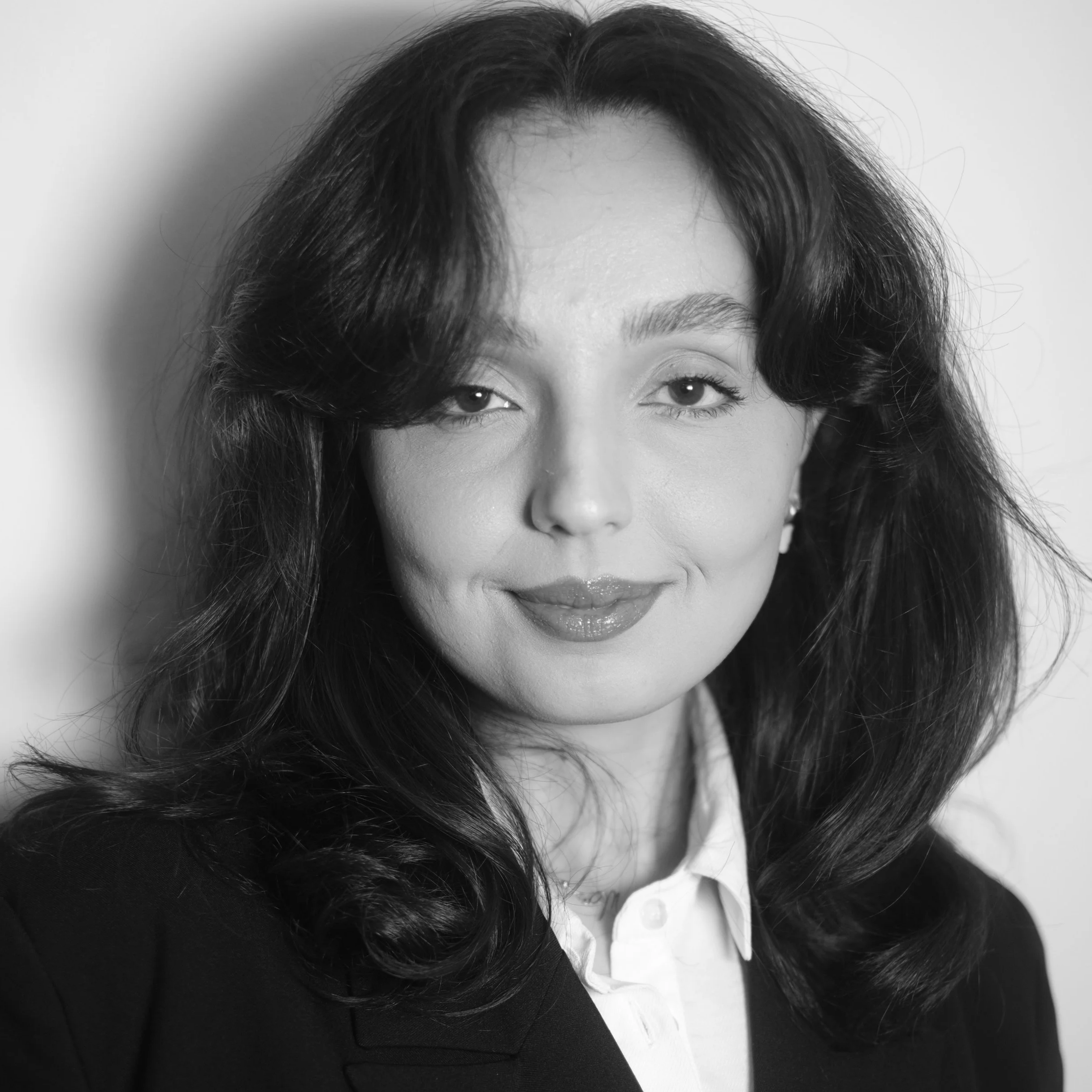 Black and white portrait of a woman with shoulder-length wavy hair, wearing a collared shirt, looking at the camera with a slight smile.