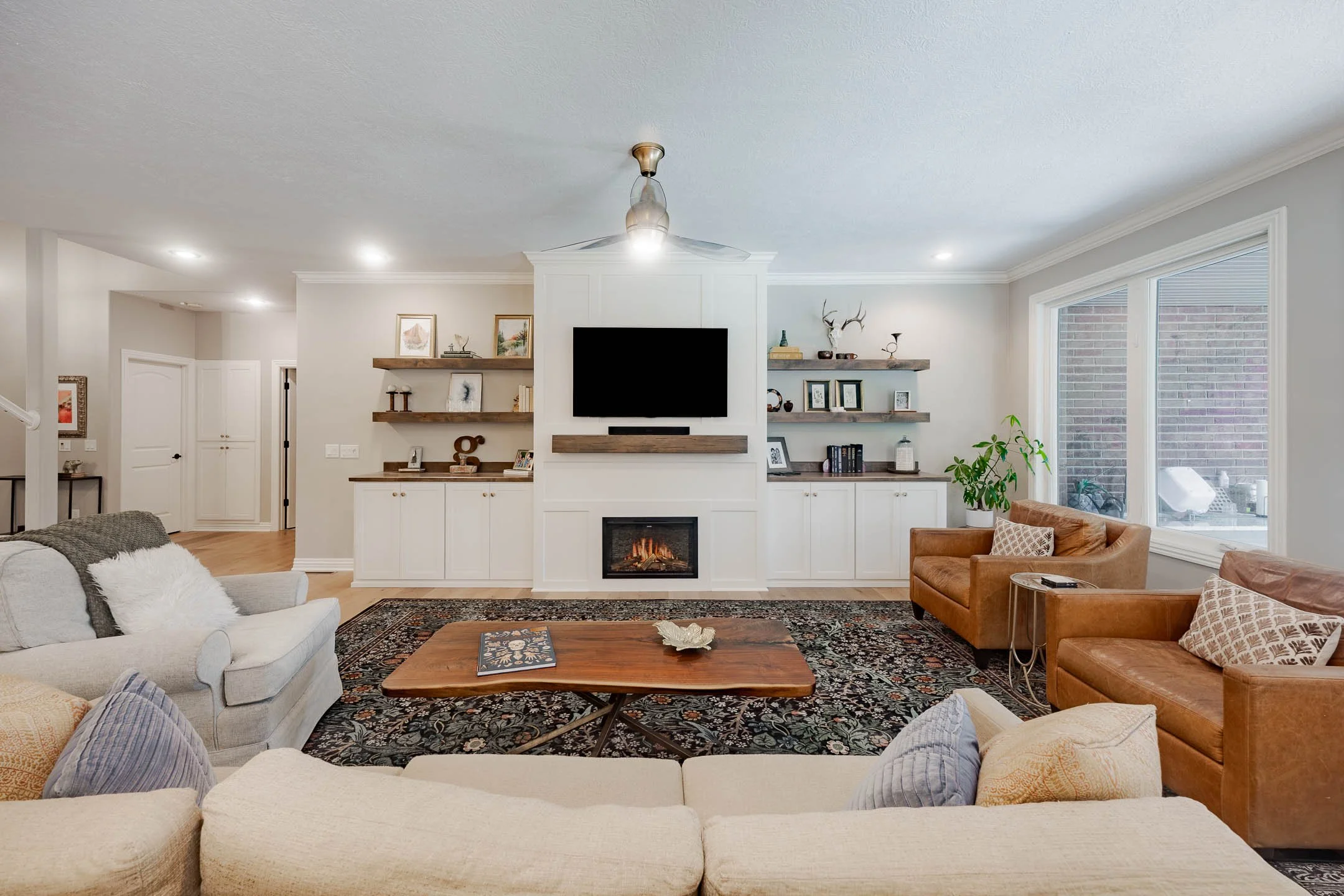 Living room with a fireplace, wall-mounted TV, patterned rug, sofa, and armchairs.