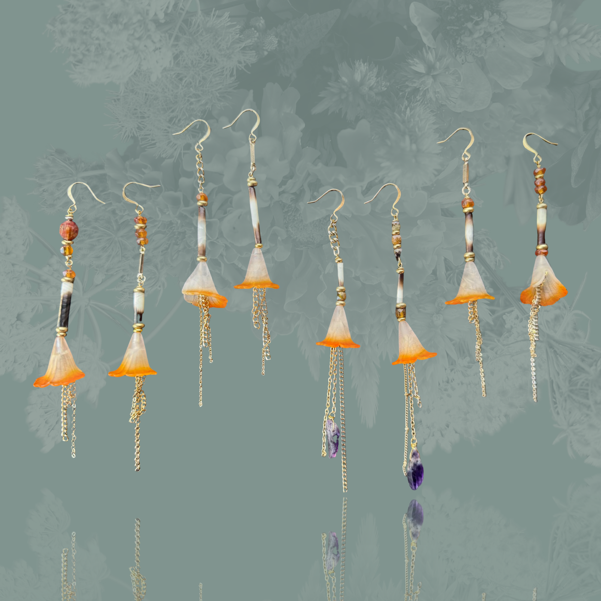 Artistic photo of handcrafted earrings featuring feather shapes, orange accents, and dangling chains, set against a textured, leafy background.