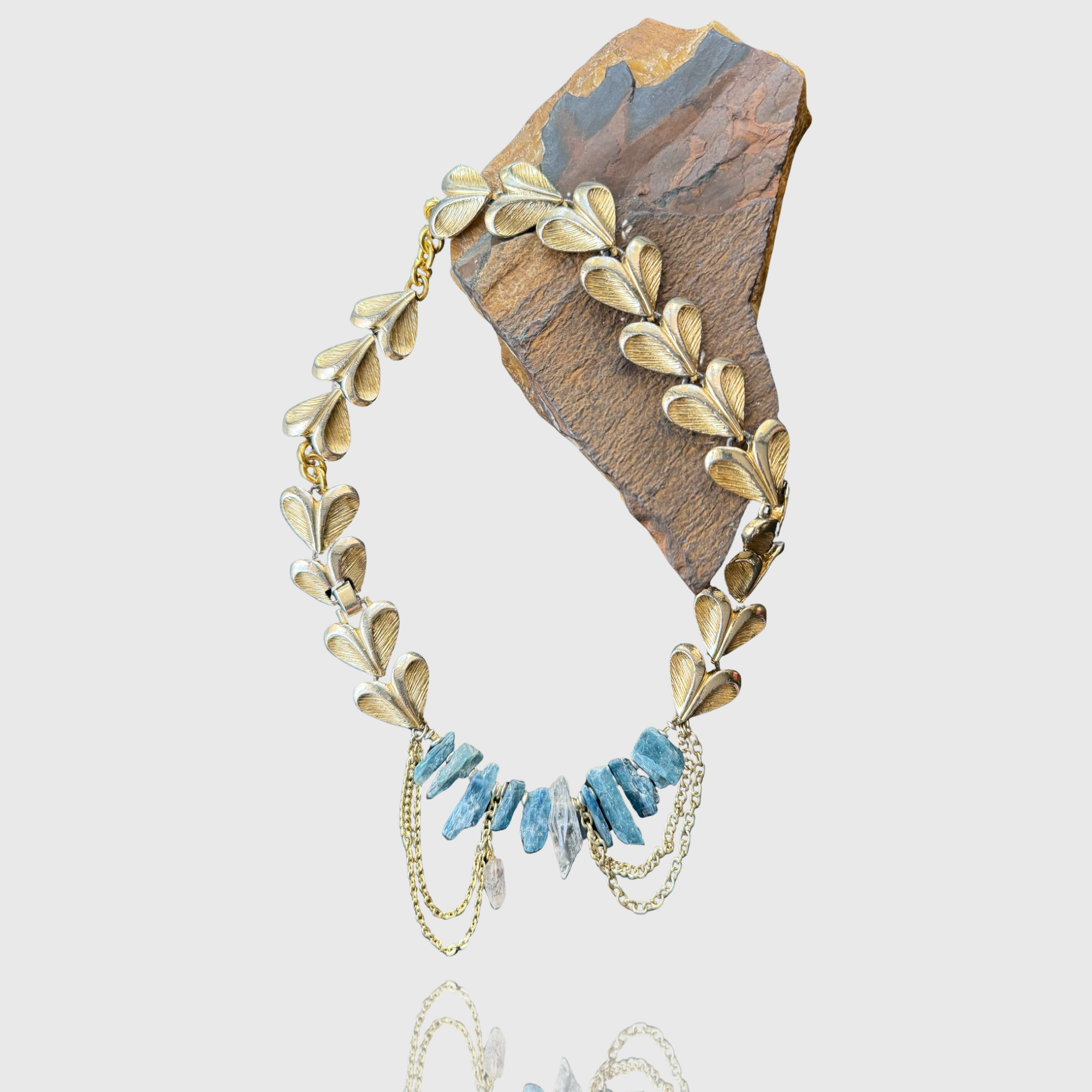Gold leaf necklace with blue gemstones and chains on a rock background.