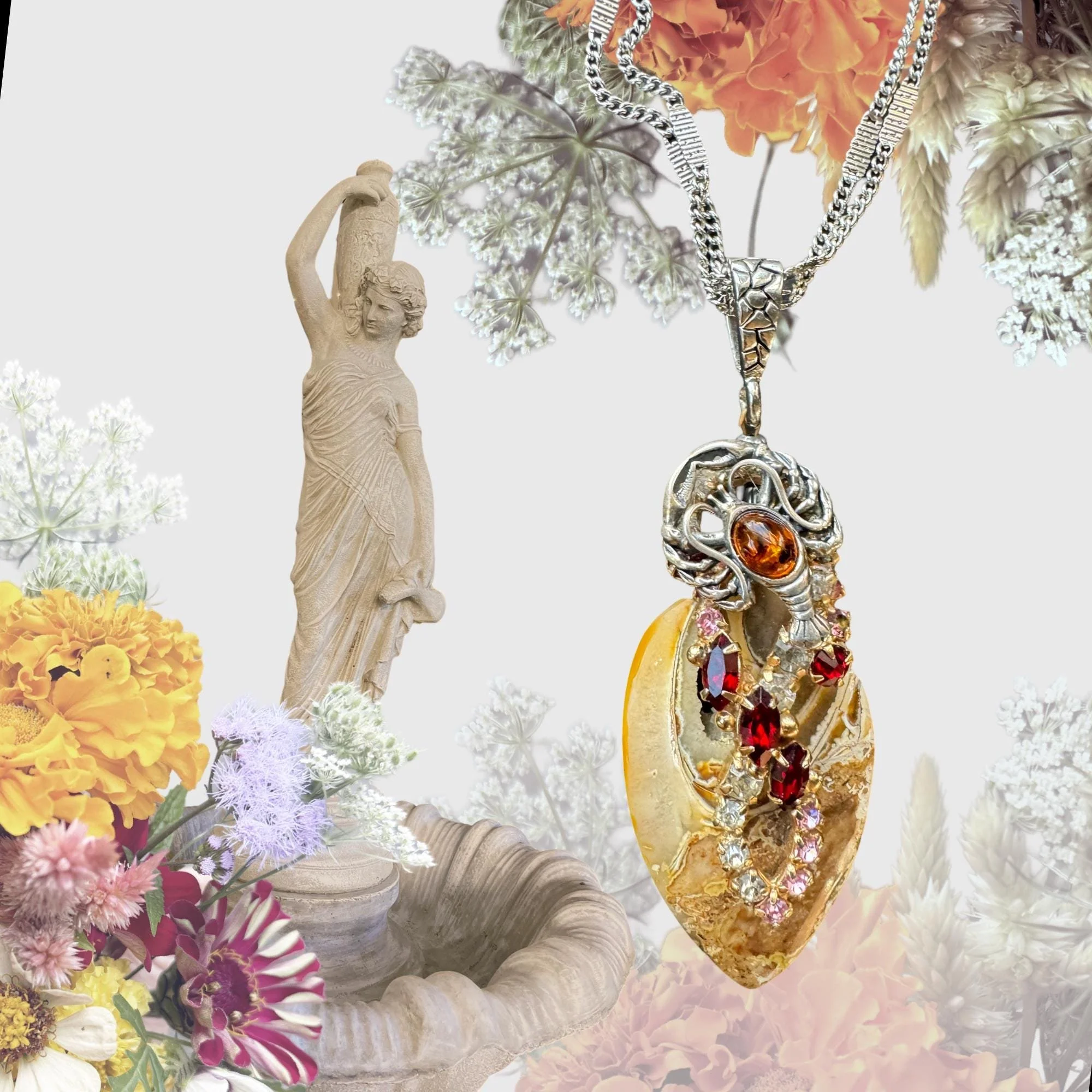 Decorative necklace with an ornate pendant featuring red and clear gems and amber stone, set against a background of a classical statue fountain surrounded by vibrant flowers.