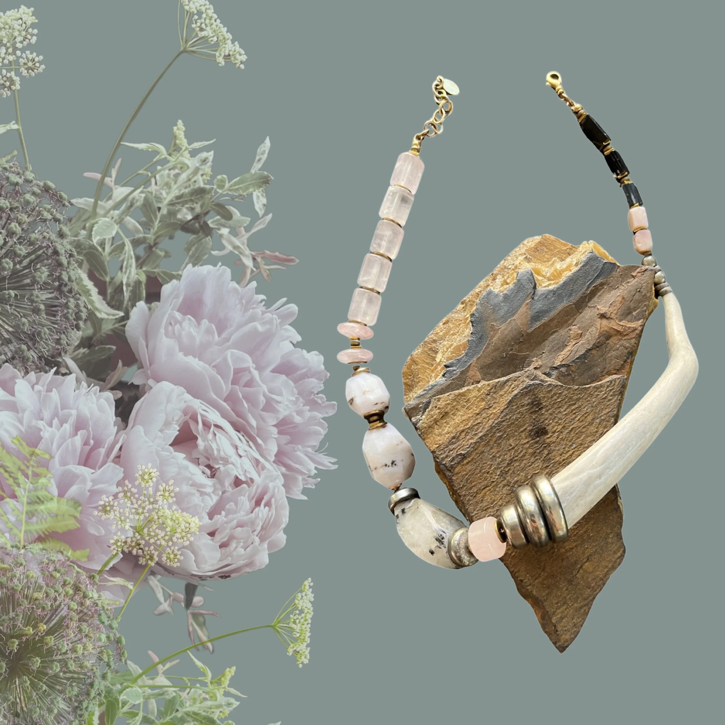 Artistic composition featuring a beaded necklace with stones and bone, paired with a floral arrangement of pink and cream flowers against a muted green background.