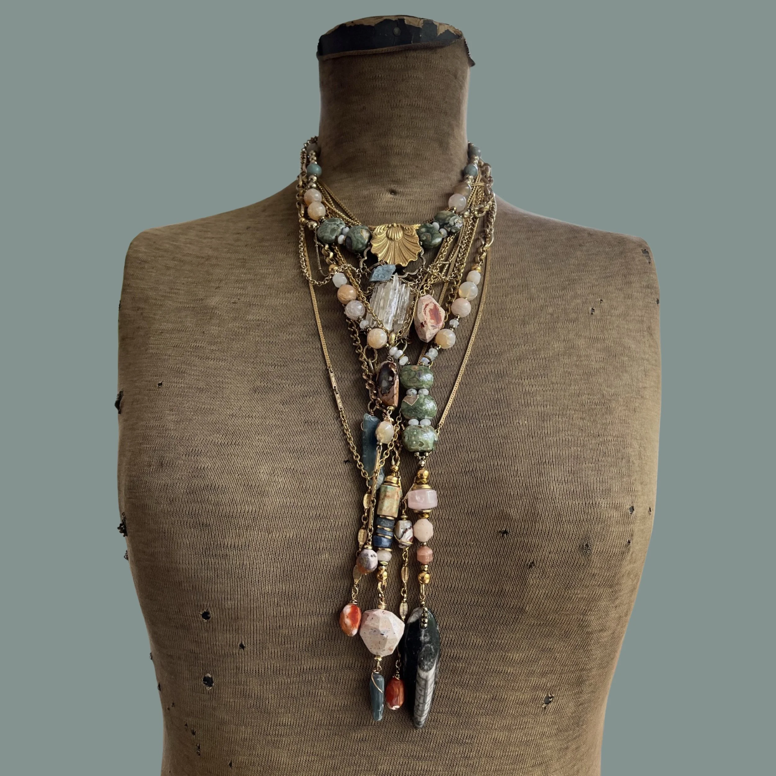 Vintage dress form with multiple layered necklaces featuring beads, chains, and pendants on a neutral background.