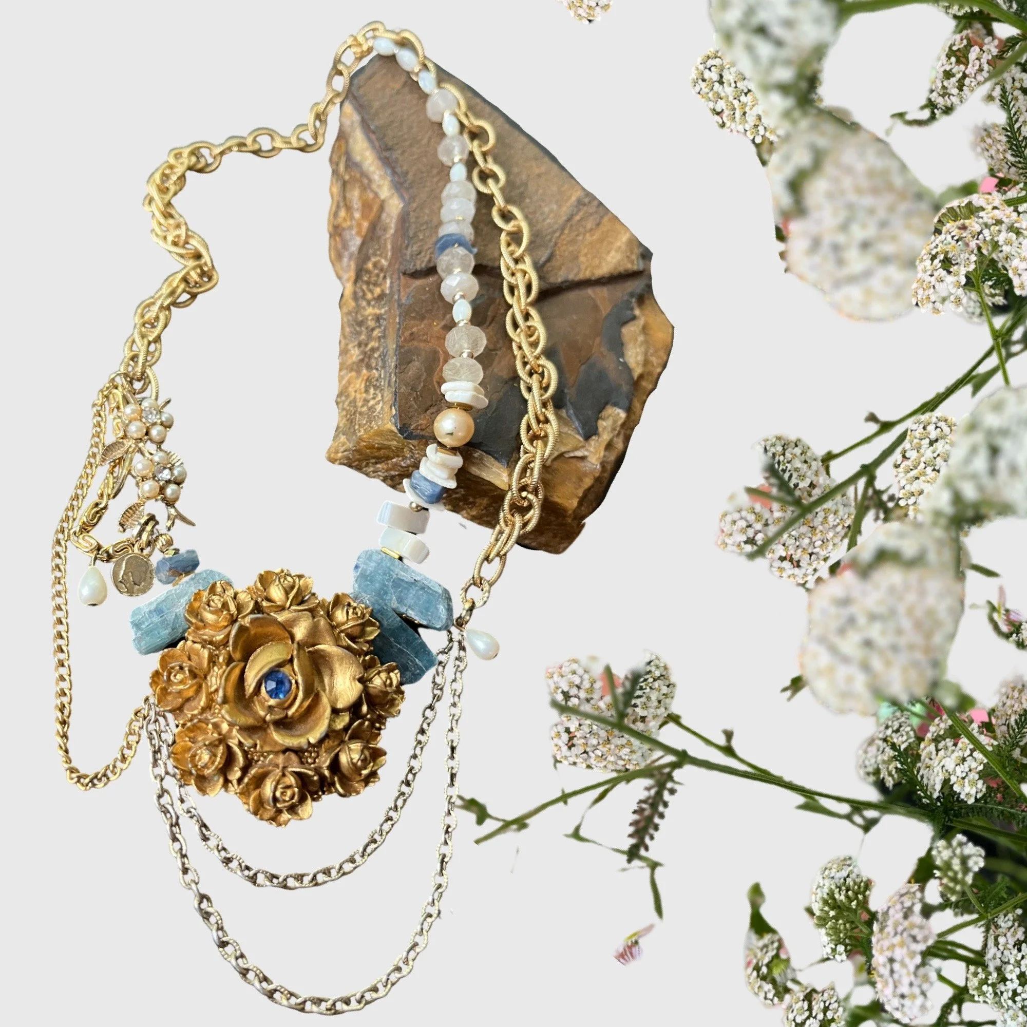 Decorative necklace with gold and blue stones on a rock with flowers.