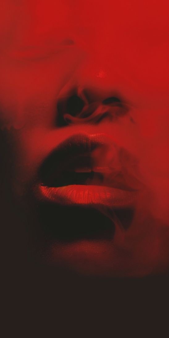 Close-up of a woman's face with red lighting, focusing on her lips, nose, and part of her eyes, with a smoky effect.