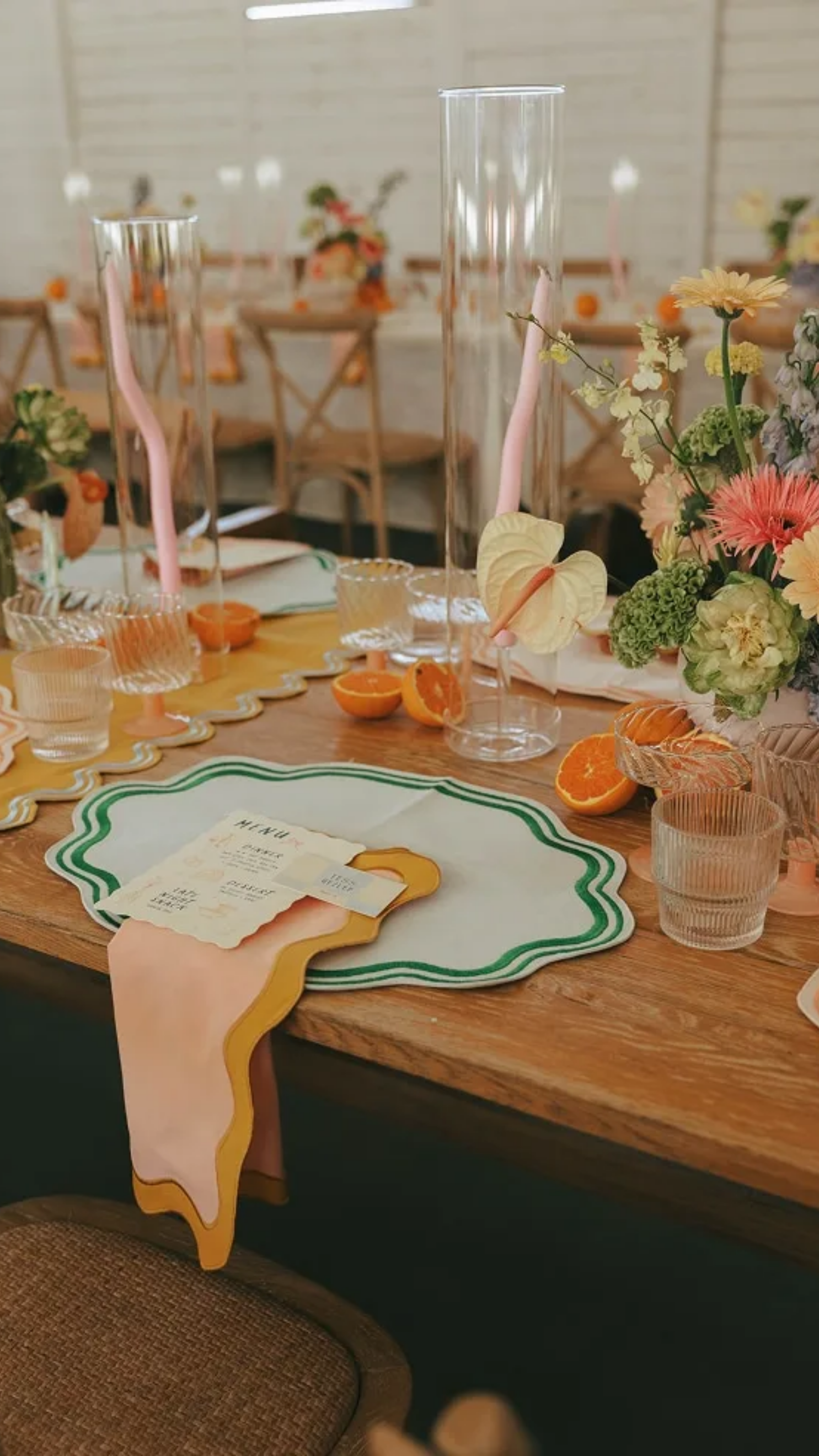 A decorated table with floral centerpieces, tall glass candle holders, umbrellas, halved oranges, and a colorful menu resembling a dripping ice cream cone.