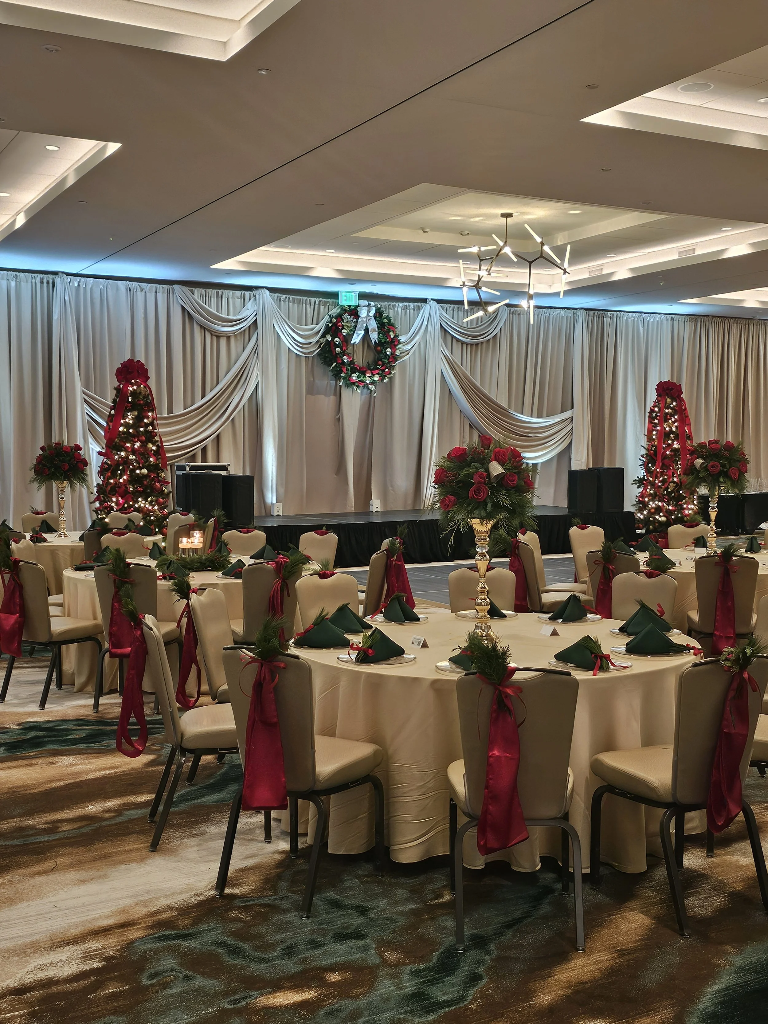 Decorated banquet hall with a stage, Christmas wreath, and tables with green napkins and red ribbons.