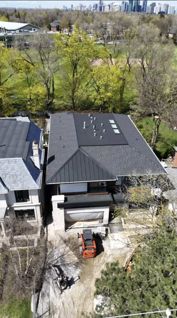 Bird's-eye view of a modern house with a flat roof on a residential street, surrounded by trees and neighboring houses, with a red vehicle parked in the driveway and a person riding a bike nearby.