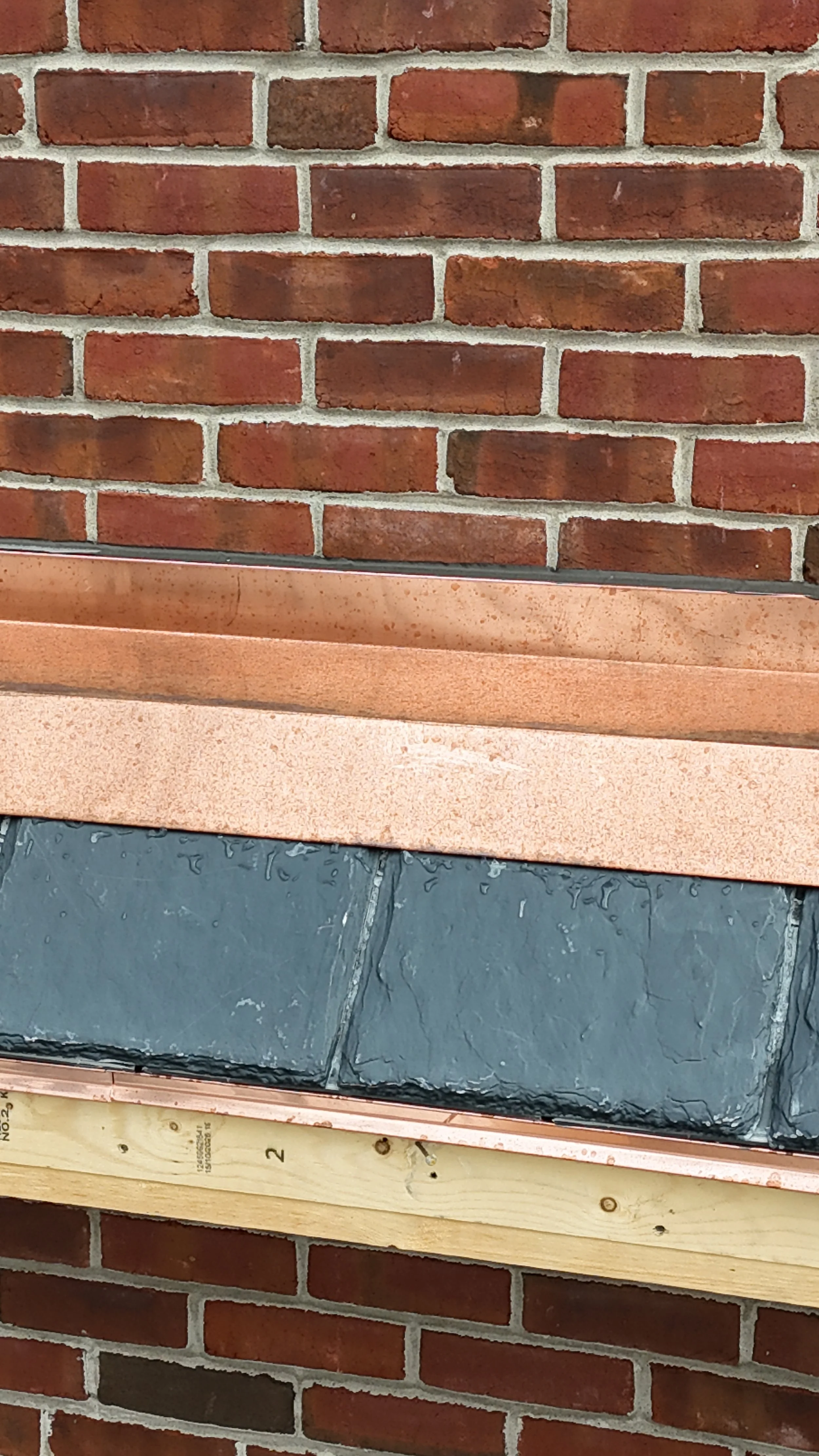 Close-up of a brick wall with a copper flashing and slate tiles being installed.