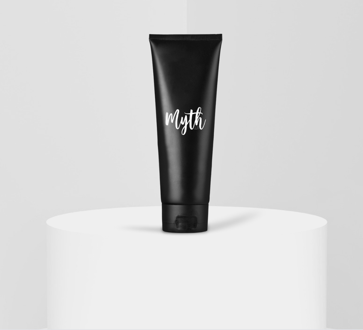 A black tube of skincare or cosmetic product labeled Myth, standing upright on a white cylindrical platform against a light gray background.