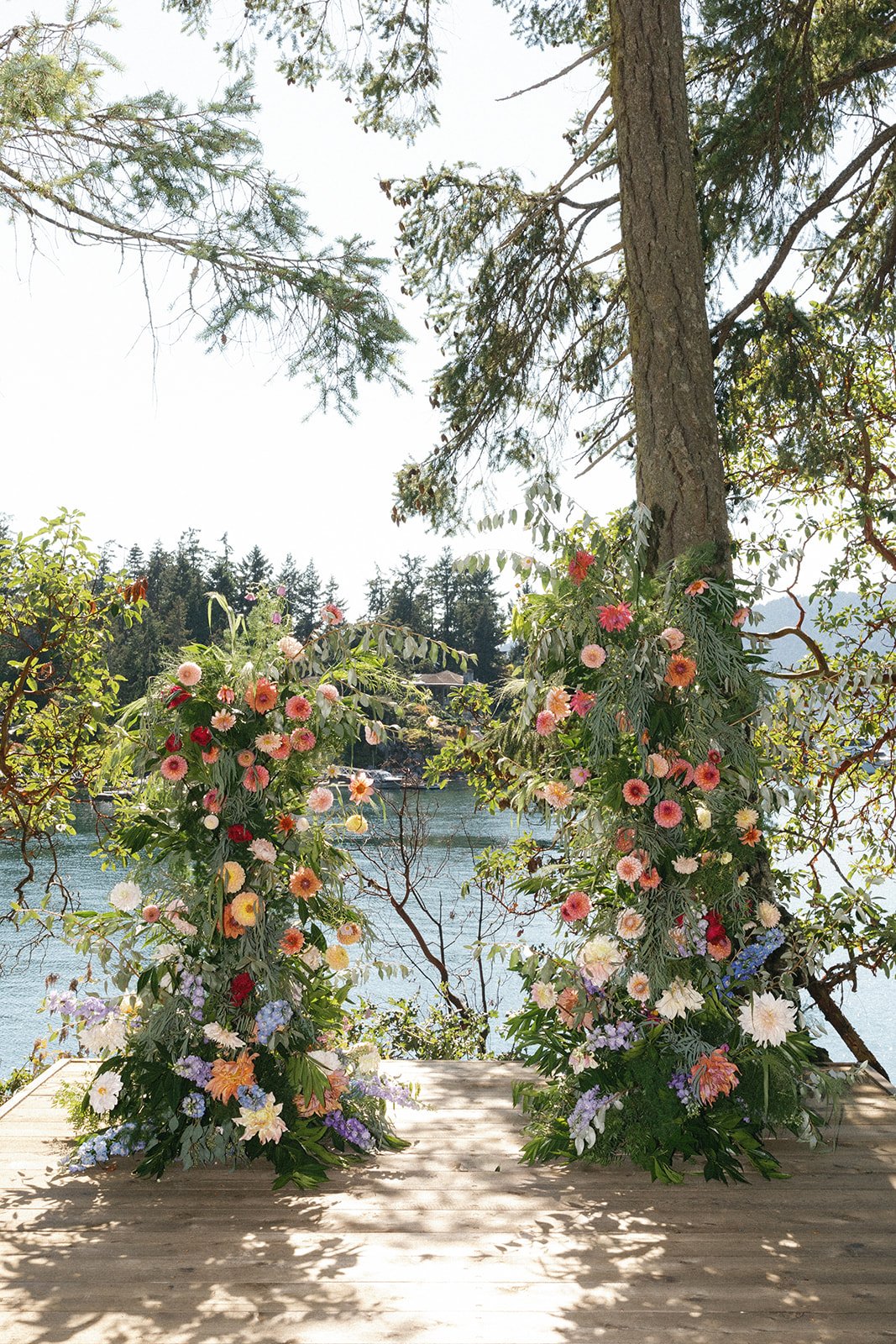 Two floral arrangements with colorful flowers by a lake, surrounded by trees, under a clear sky.